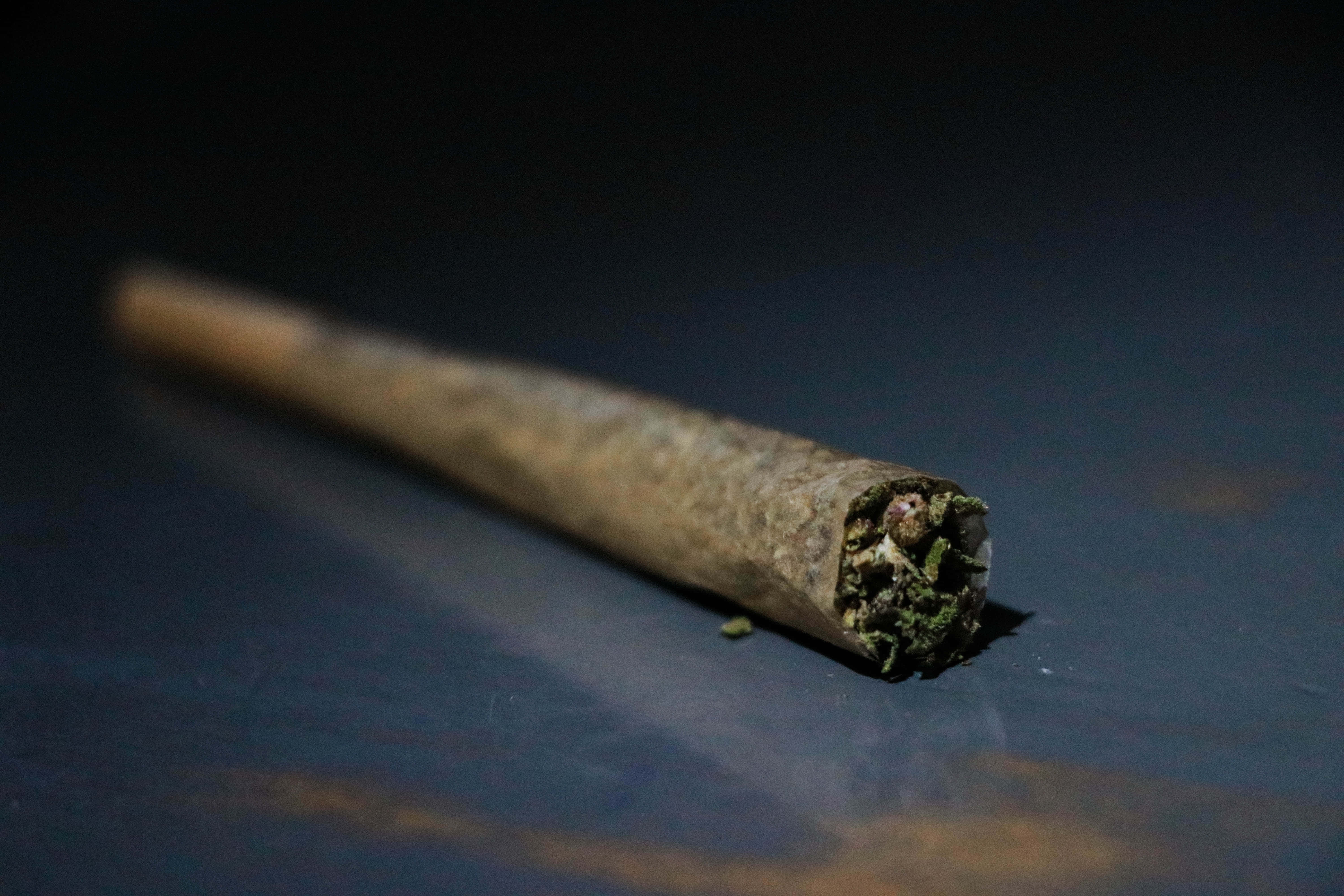 Weed Blunt 桌布 壁紙 — 一個已點燃的大麻煙捲特寫，放置在深色反光表面上，光線柔和。