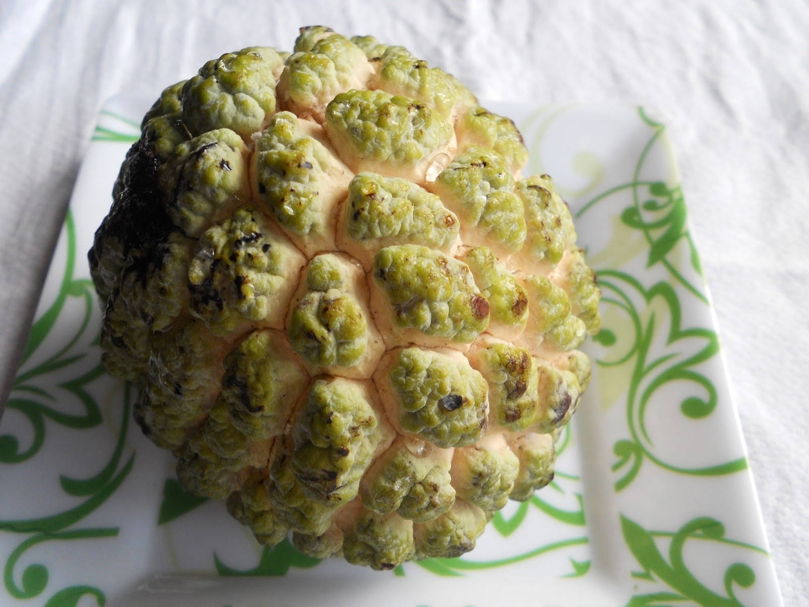 Fruit 桌布 壁紙 — 一個帶刺的綠色奶油蘋果放在帶有綠色花卉圖案的白色盤子上的特寫。