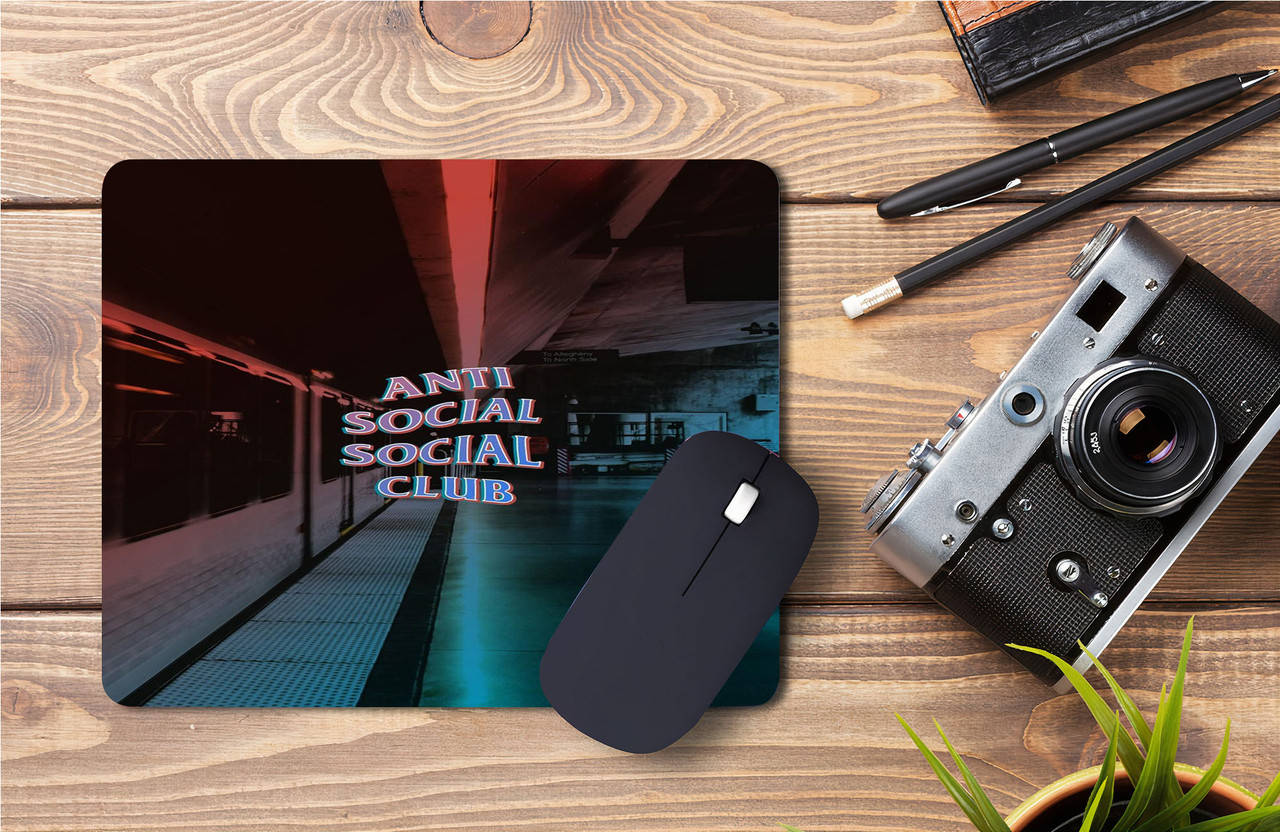 club 桌布 壁紙 — 一個帶有 'Anti Social Social Club' 霓虹燈牌的地鐵站台滑鼠墊，放在木桌上，旁邊有一台復古相機和筆。