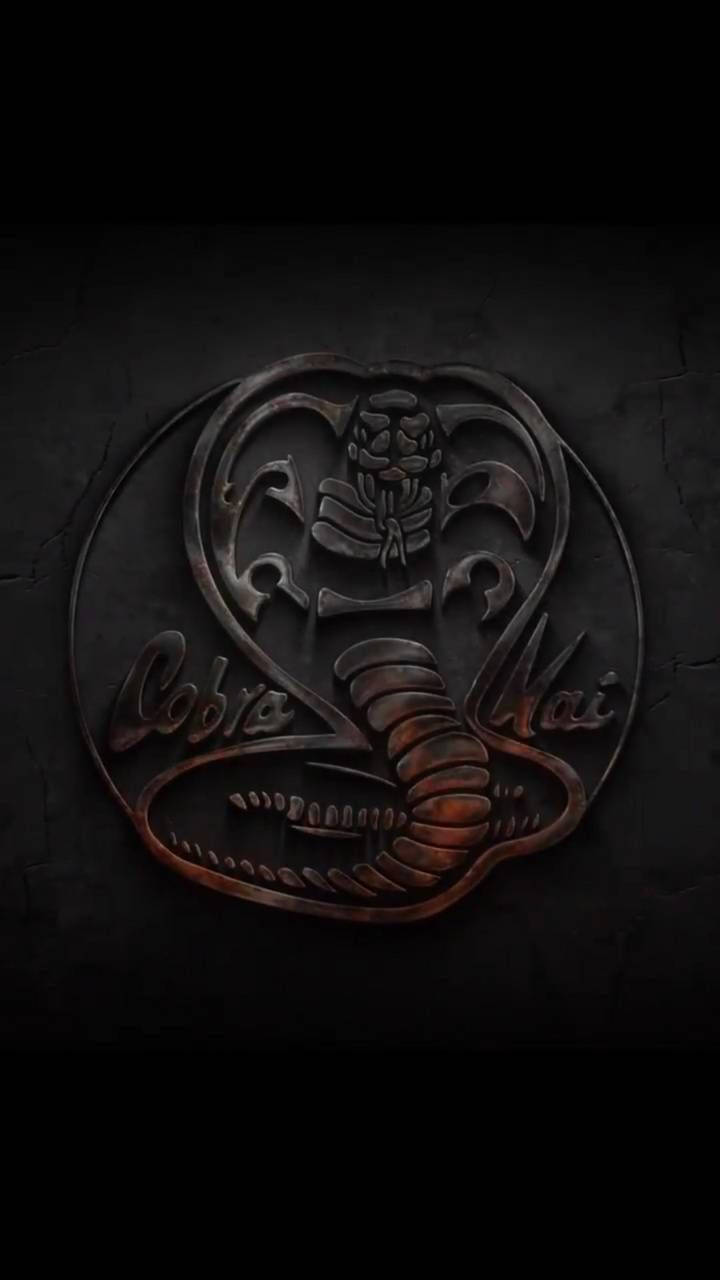 Cobra Kai Phone 桌布 壁紙 — 一個帶有 'Cobra Kai' 文字的威脅性金屬眼鏡蛇標誌，刻在昏暗燈光下的破裂暗牆上。