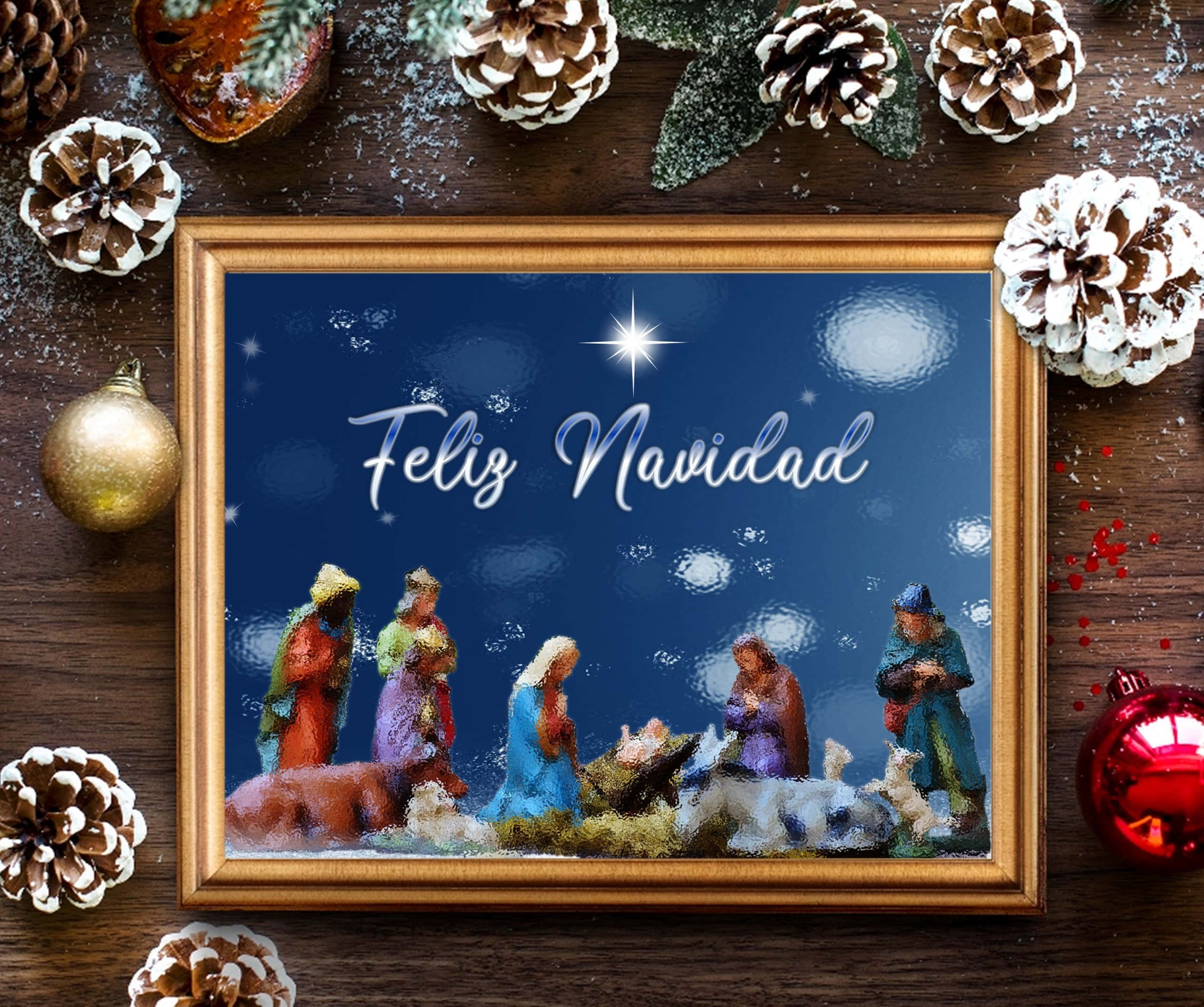 Religious Christmas 桌布 壁紙 — 一個帶有 'Feliz Navidad' 文字的裱框耶穌誕生場景，周圍環繞著松果、裝飾品和雪，置於木質表面上。