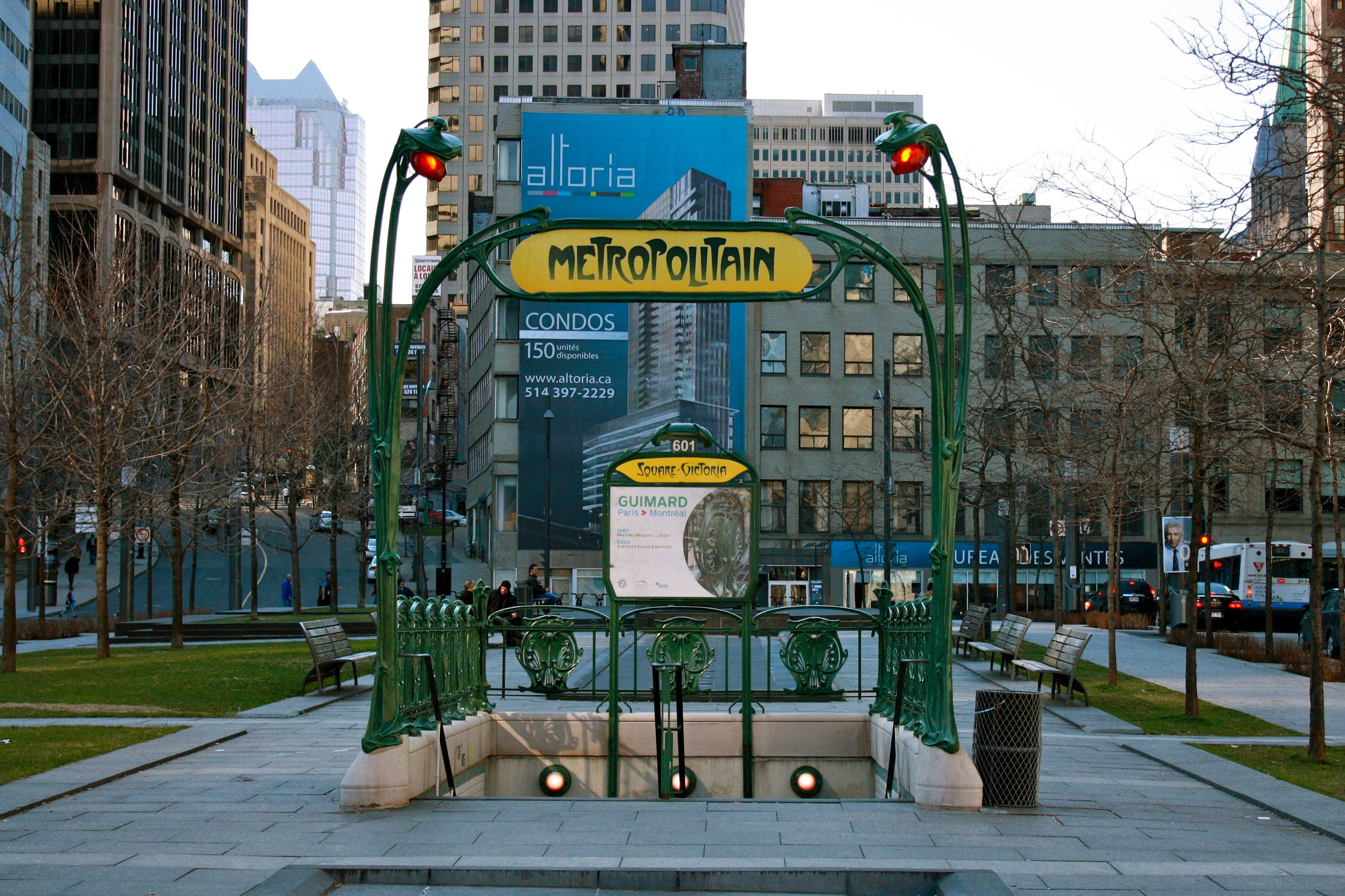 Montreal 桌布 壁紙 — 一個帶有 'METROPOLITAIN' 標誌的綠色華麗地鐵入口，矗立在黃昏時分的城市廣場上，周圍是高樓大廈和光禿禿的樹木。