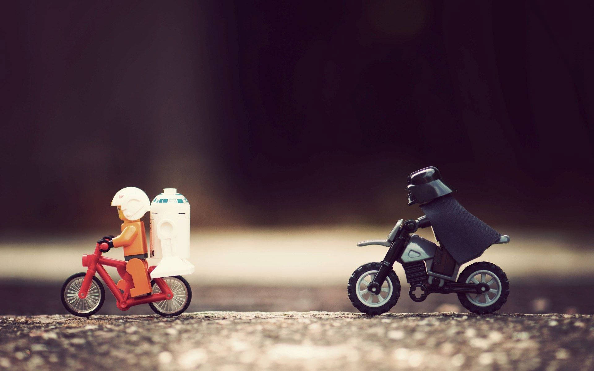 樂高 桌布 壁紙 — 一個帶有R2-D2的LEGO人偶騎著紅色腳踏車，而達斯維達則騎著黑色摩托車在碎石路上行駛。