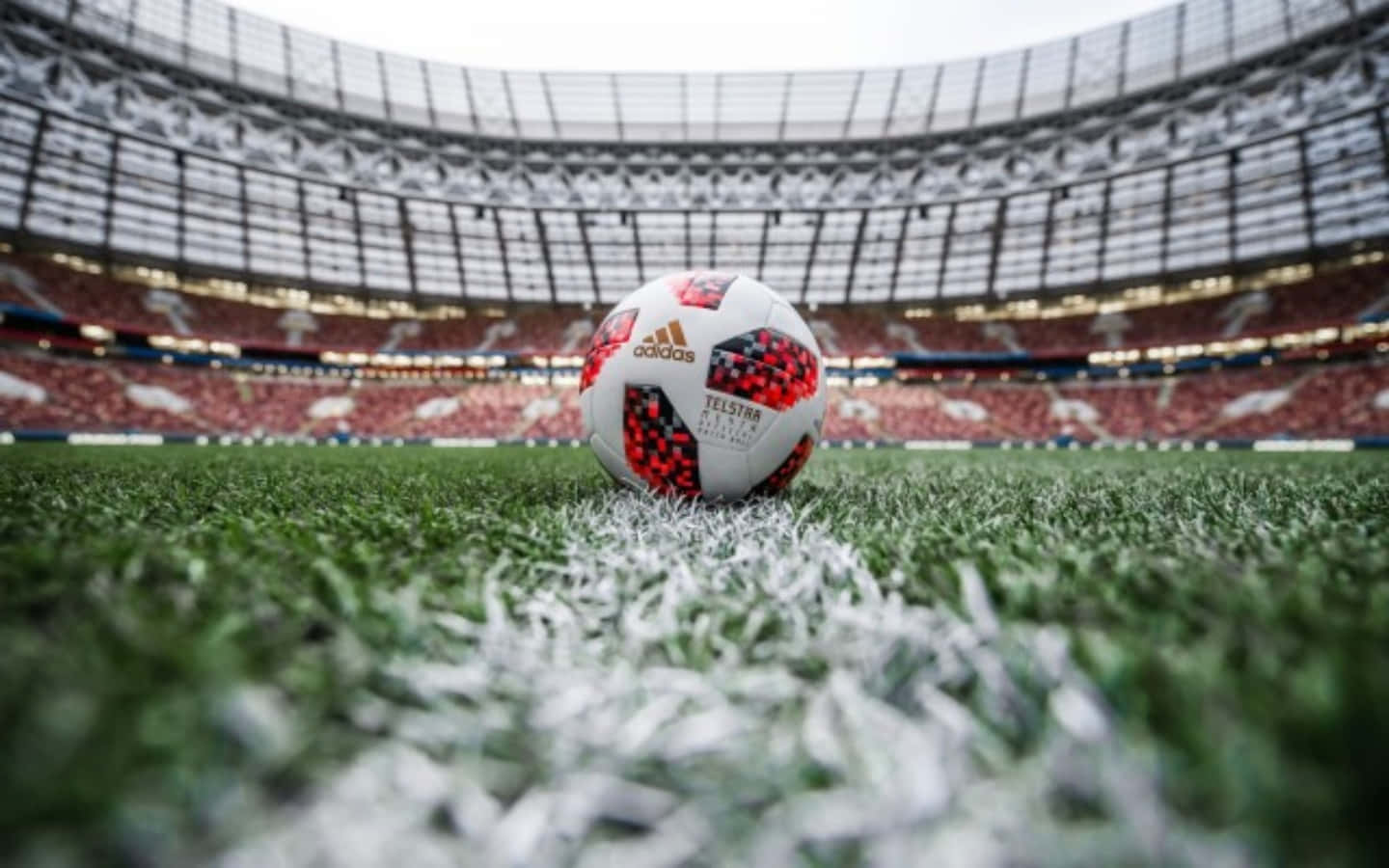 Soccer Ball 桌布 壁紙 — 一個帶有Telstra標誌的足球放在充滿活力的綠色草地上，草地上有白色線條，球場空無一人，天空多雲。