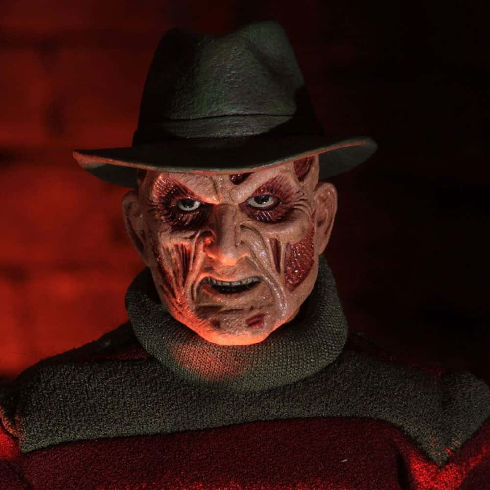 Freddy Krueger 桌布 壁紙 — 一個帶有傷疤臉和帽子的恐怖佛萊迪·克魯格人偶，在紅光照射下對著磚牆怒視。