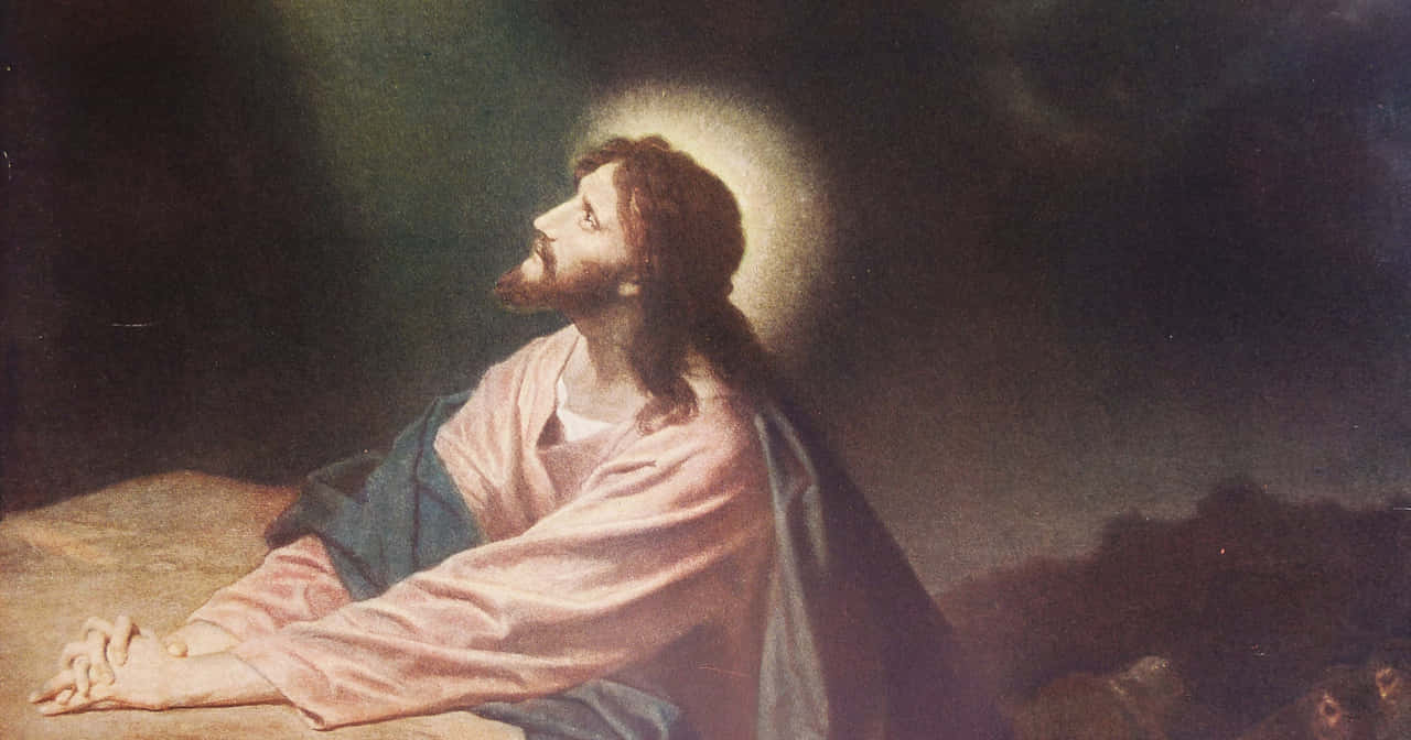 Jesus Praying 桌布 壁紙 — 一個帶有光環的莊嚴人物在黑暗背景下跪著祈禱，柔和的神聖光芒照亮他的臉龐和長袍。