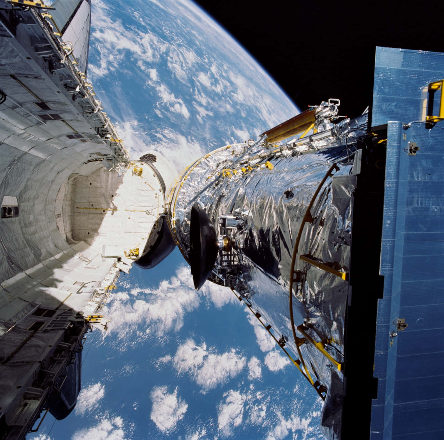 Hubble Space Telescope 桌布 壁紙 — 一個帶有反射性銀色面板和藍色太陽能板的太空望遠鏡，在太空的黑色虛空中，漂浮在地球彎曲的藍白雲層覆蓋的表面之上。