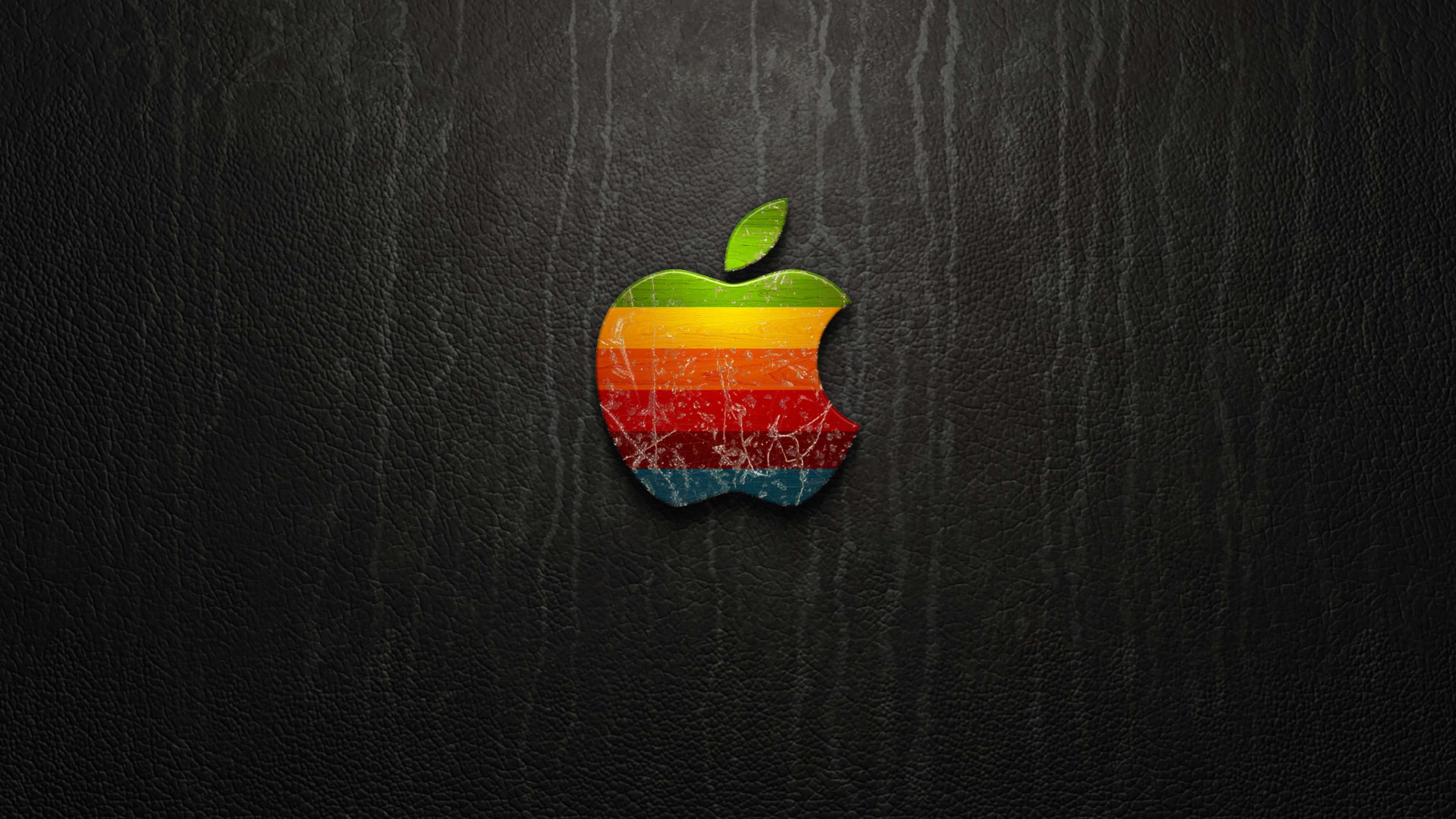 4K Apple 桌布 壁紙 — 一個帶有咬痕的復古彩虹Apple標誌放置在深色紋理皮革表面上。