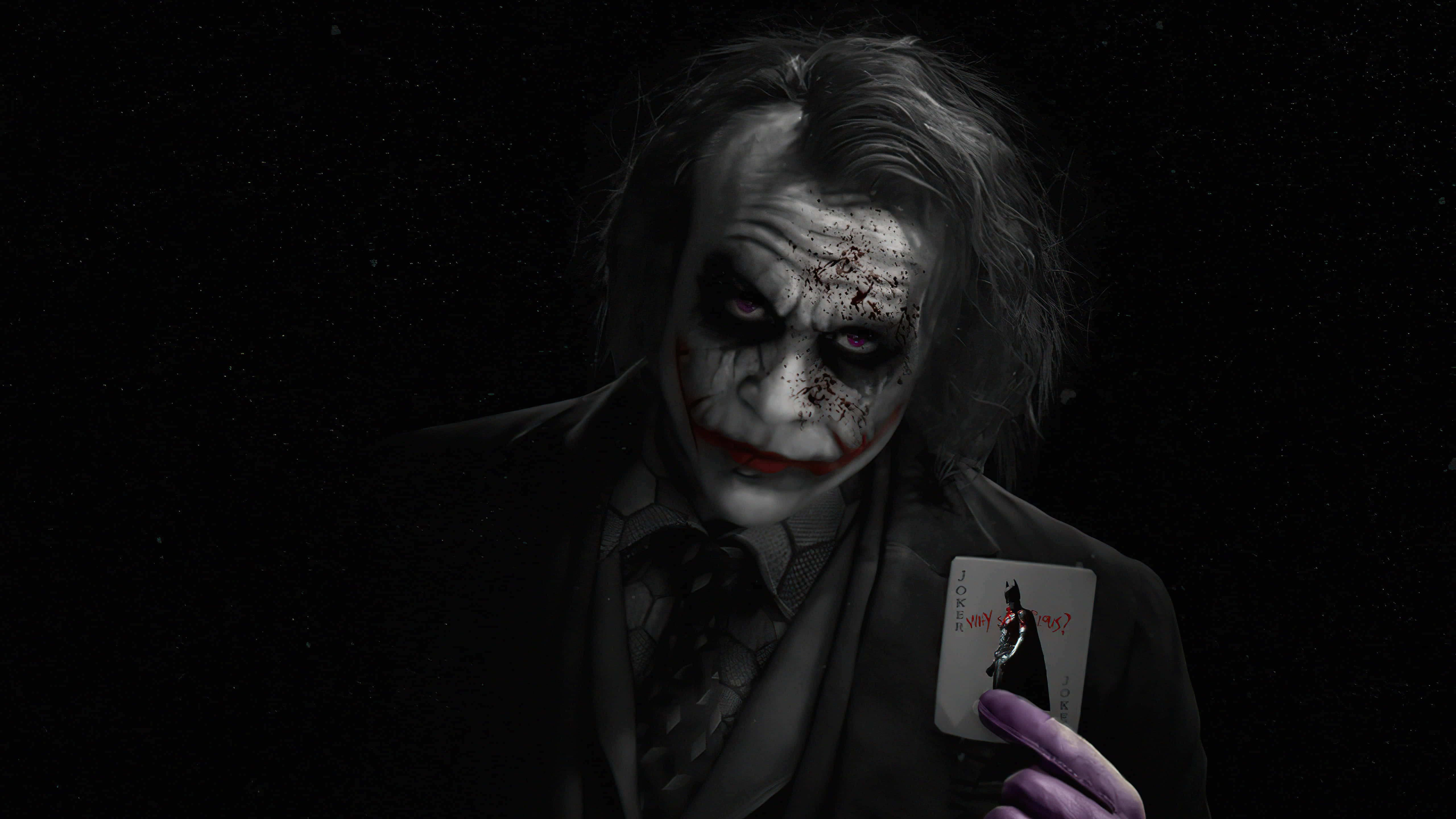 Joker Card 桌布 壁紙 — 一個帶有塗抹白色臉部化妝和紅唇的威脅性小丑，在黑色背景前拿著一張小丑牌。