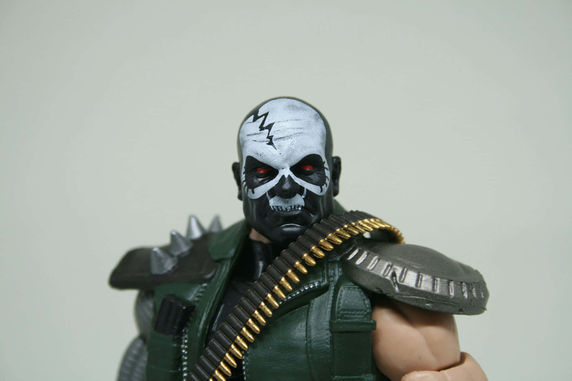 Skullbuster 桌布 壁紙 — 一個帶有威脅性的動作人偶，戴著骷髏面具、紅色眼睛，穿著綠色背心並配有金色彈藥帶，背景為純色。