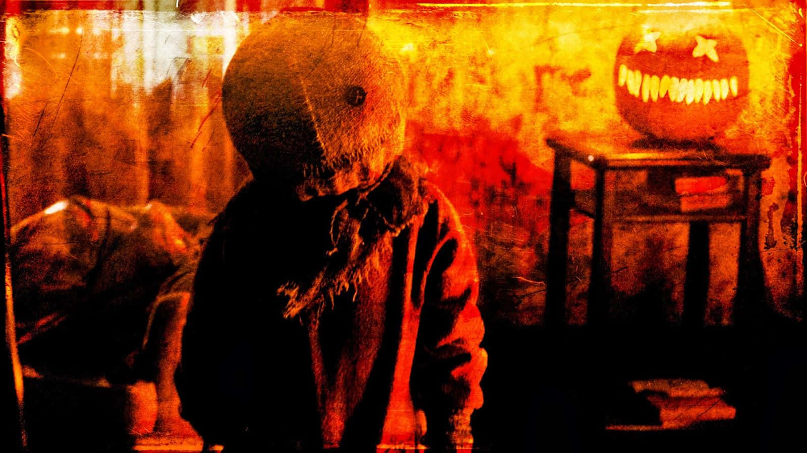 恐怖電影 桌布 壁紙 — 一個帶有威脅性的縫合娃娃站在燈光昏暗的房間裡，桌上發光的傑克南瓜燈投射出詭異的橙色光芒。