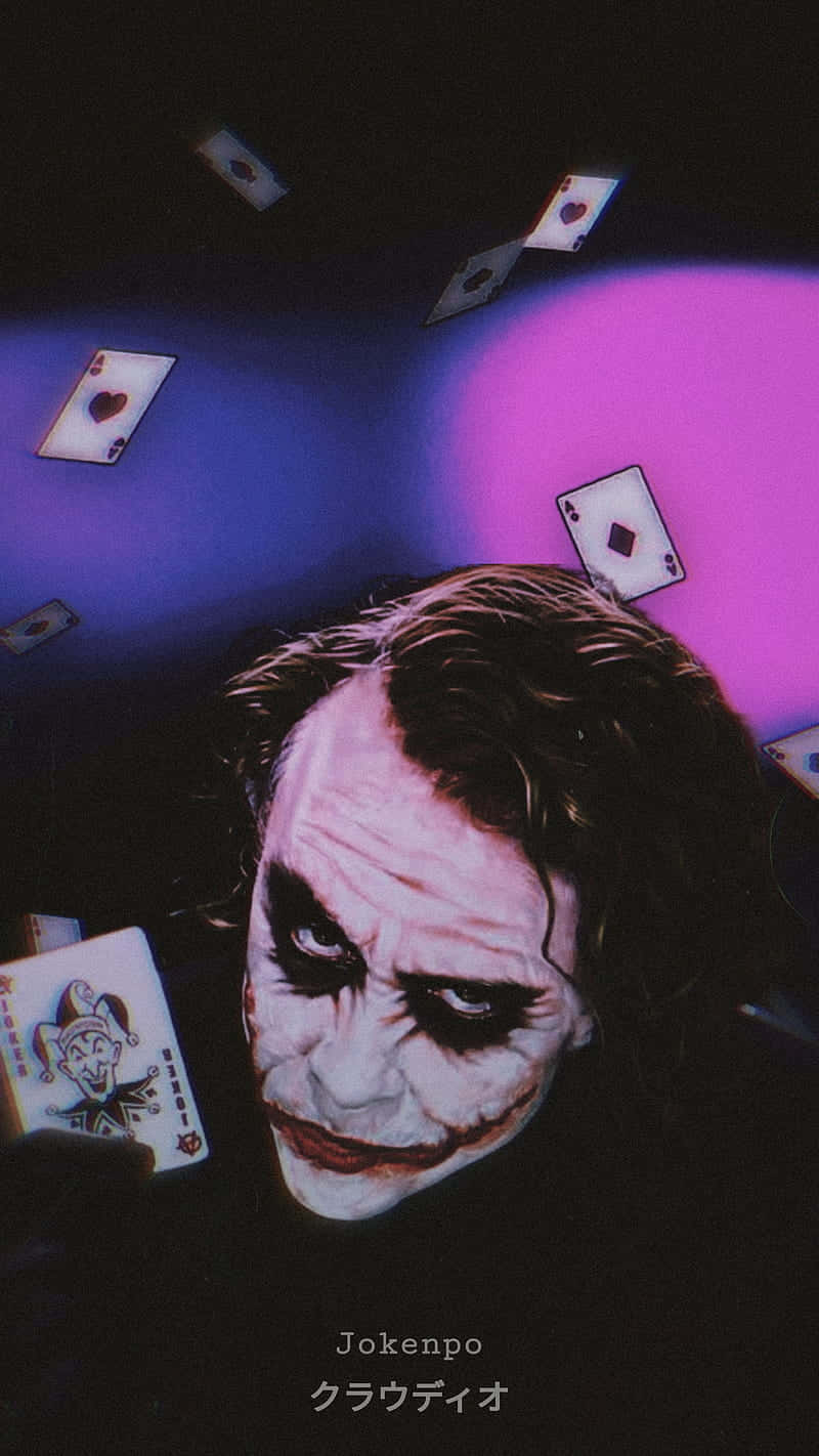 桌布 壁紙 — 一個帶有寬闊笑容的威脅性小丑向上凝視，周圍漂浮著撲克牌，在紫色和藍色燈光下。