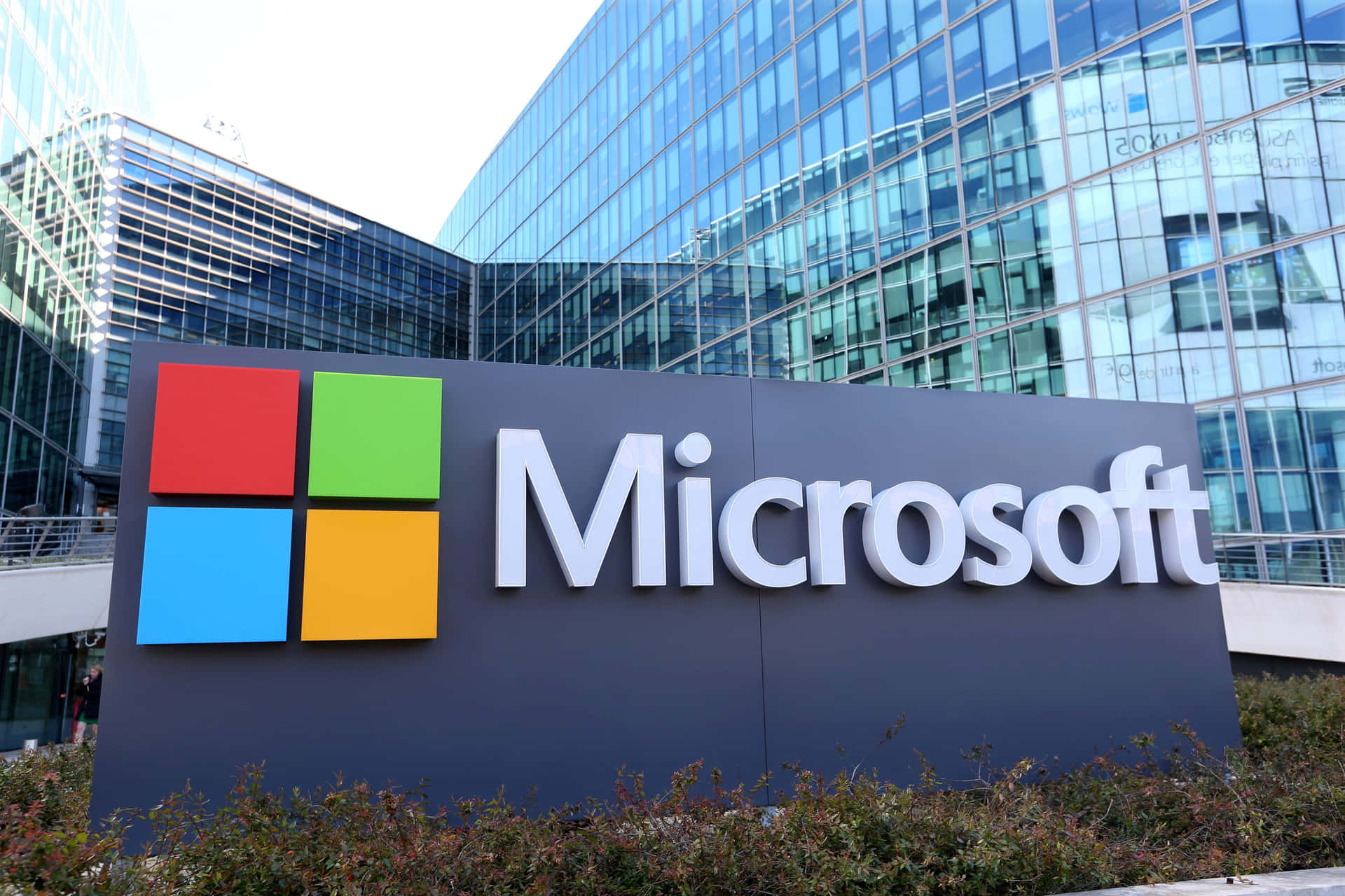 Microsoft公司標誌牌，帶有彩色標誌，位於玻璃辦公樓前。 — Microsoft 壁紙