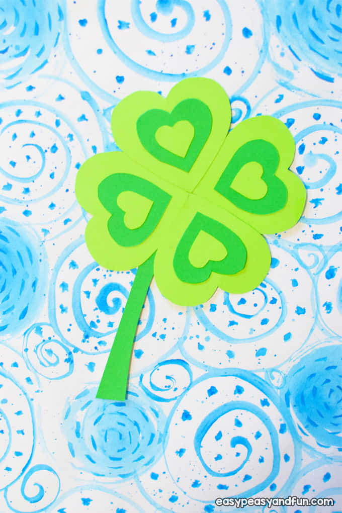 Four Leaf Clover 桌布 壁紙 — 一個帶有心形鏤空的亮綠色紙製四葉草，放置在藍色漩渦和潑濺塗鴉背景上。