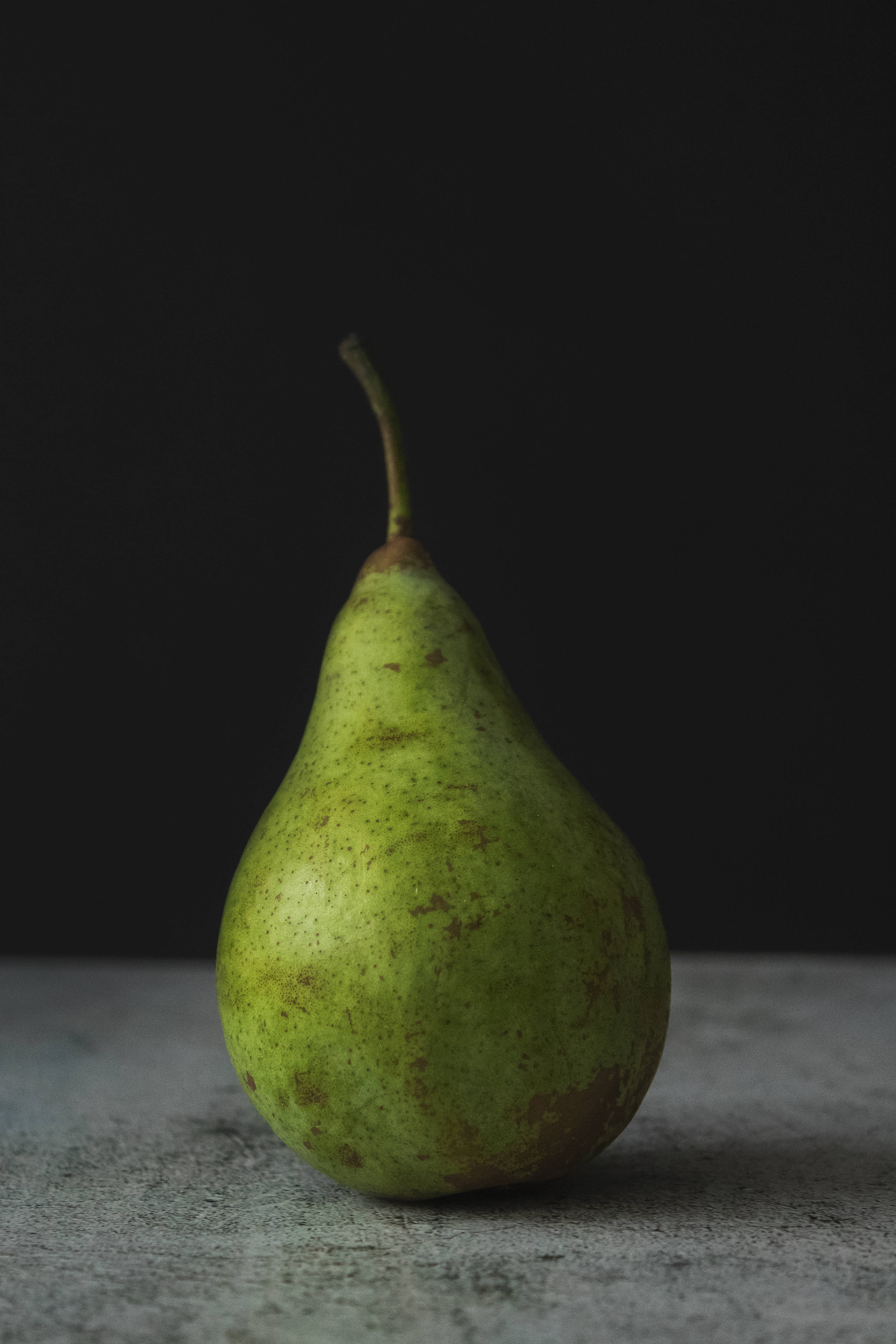 Fruit 桌布 壁紙 — 一個帶有斑點的綠色梨子放在紋理灰色表面上，背景為深色。