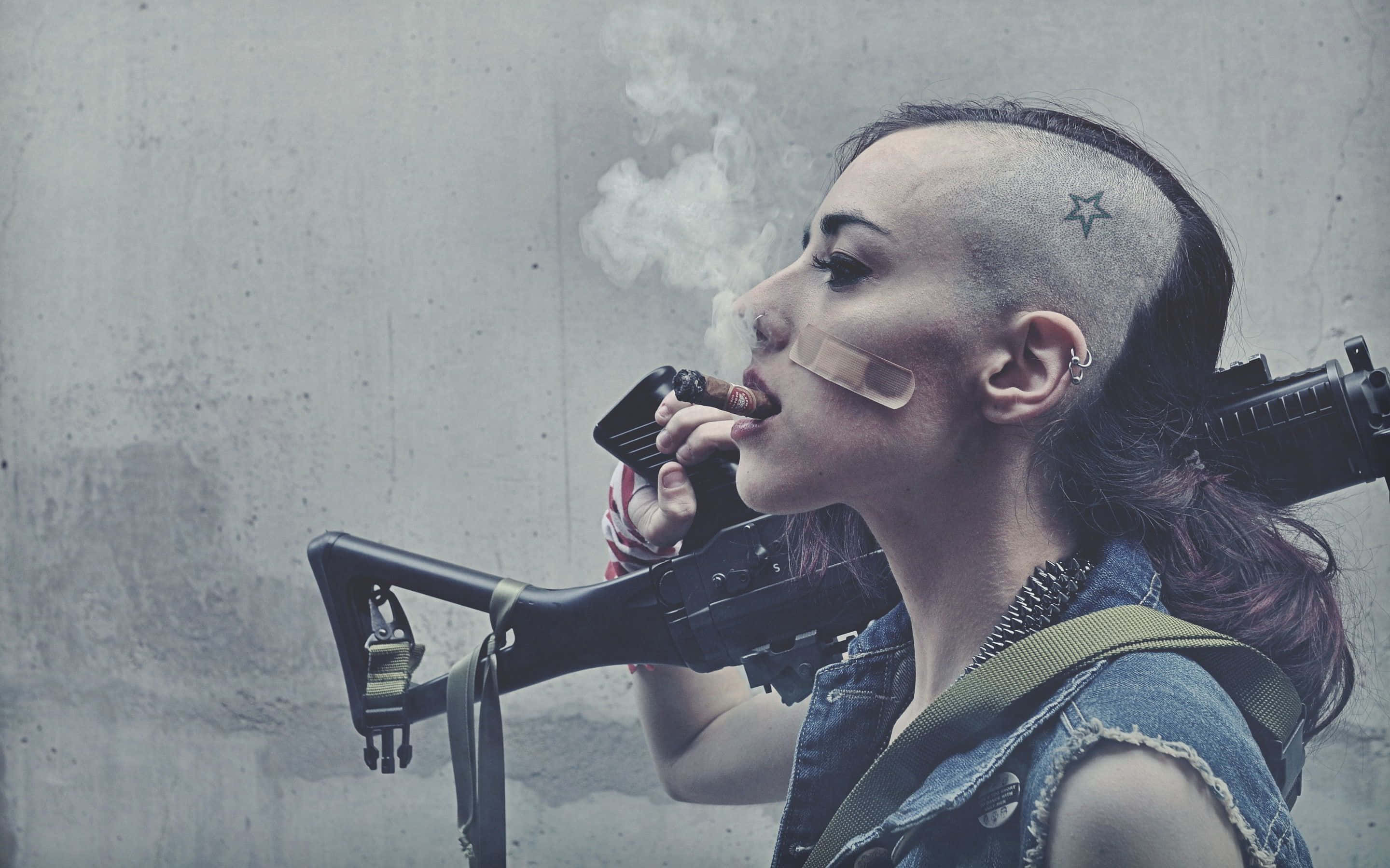 Girl Smoking 桌布 壁紙 — 一個帶有星星刺青的兇猛女人，一邊抽雪茄，一邊拿著步槍靠在混凝土牆上。