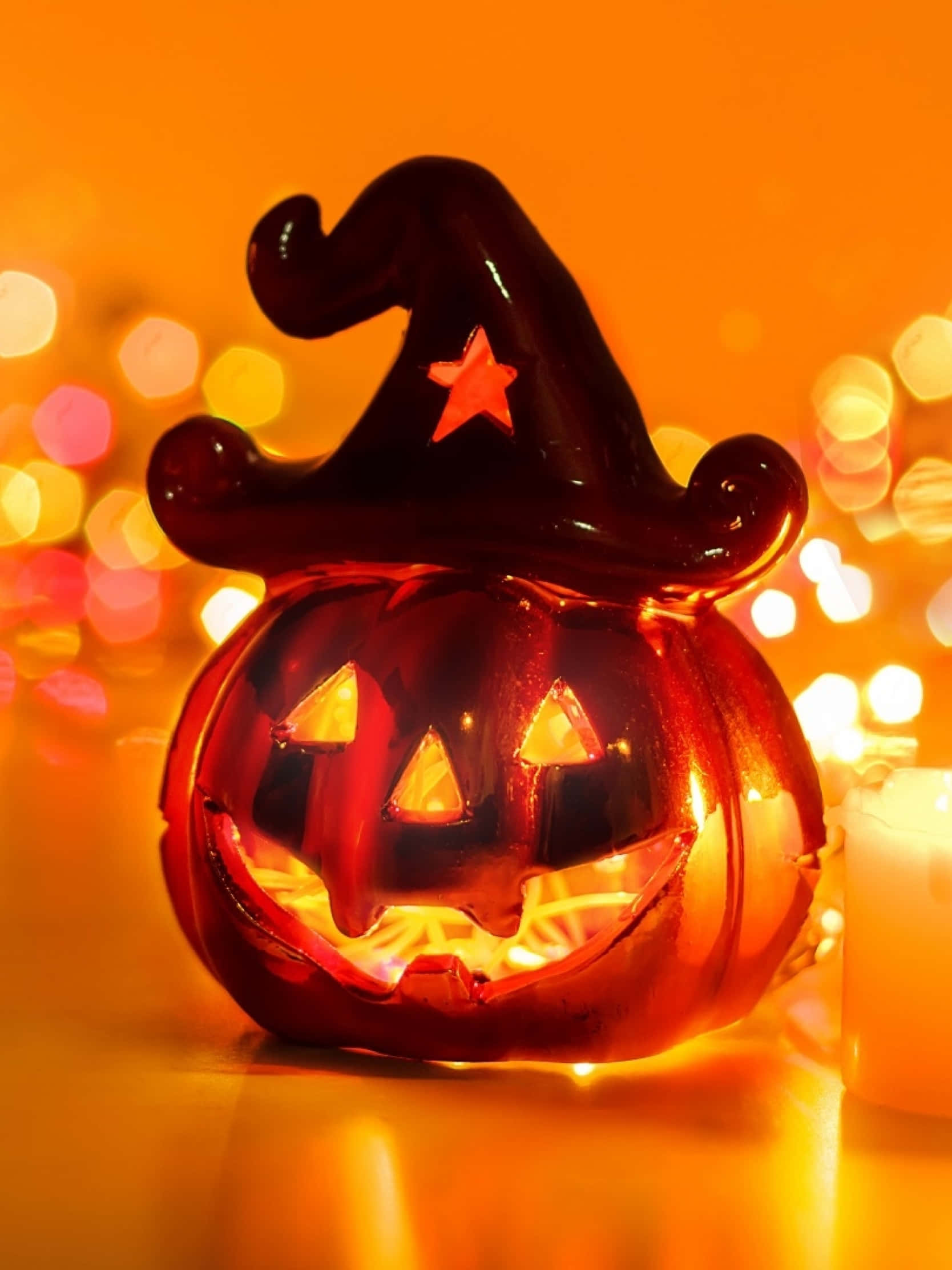 Halloween Profile 桌布 壁紙 — 一個帶有星星細節的發光紅色女巫帽南瓜燈籠，在節日燈光的散景背景下散發出溫暖的光芒。