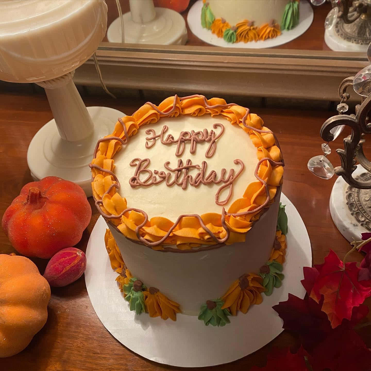 Fall Birthday 桌布 壁紙 — 一個帶有橙色和棕色裱花糖霜及秋葉的生日蛋糕，放在木桌上，旁邊有南瓜和紅葉。