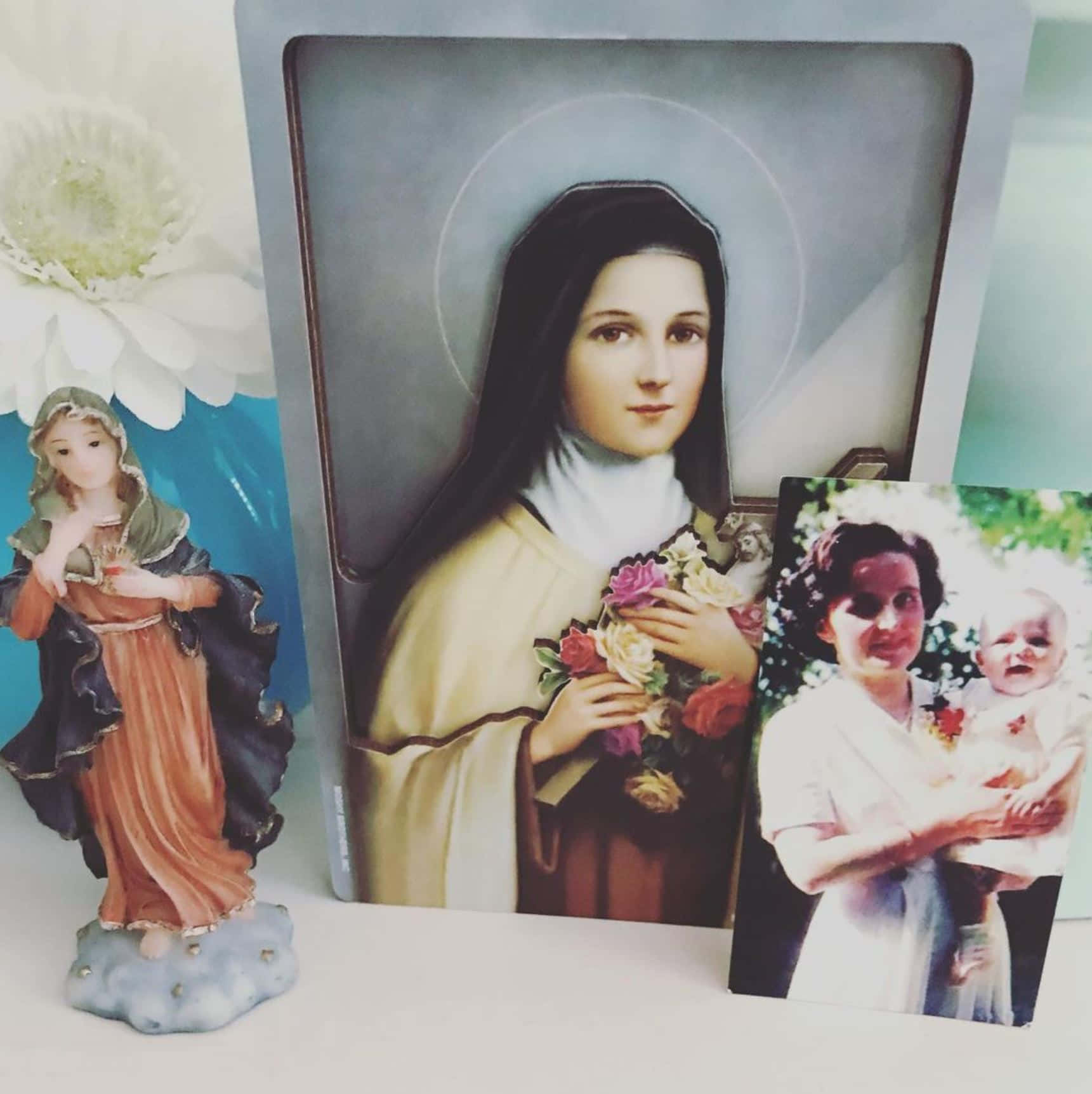 Mother Mary 桌布 壁紙 — 一個帶有玫瑰的聖人鑲框肖像，旁邊是一張女人抱著嬰兒的復古照片和一個陶瓷宗教小雕像。