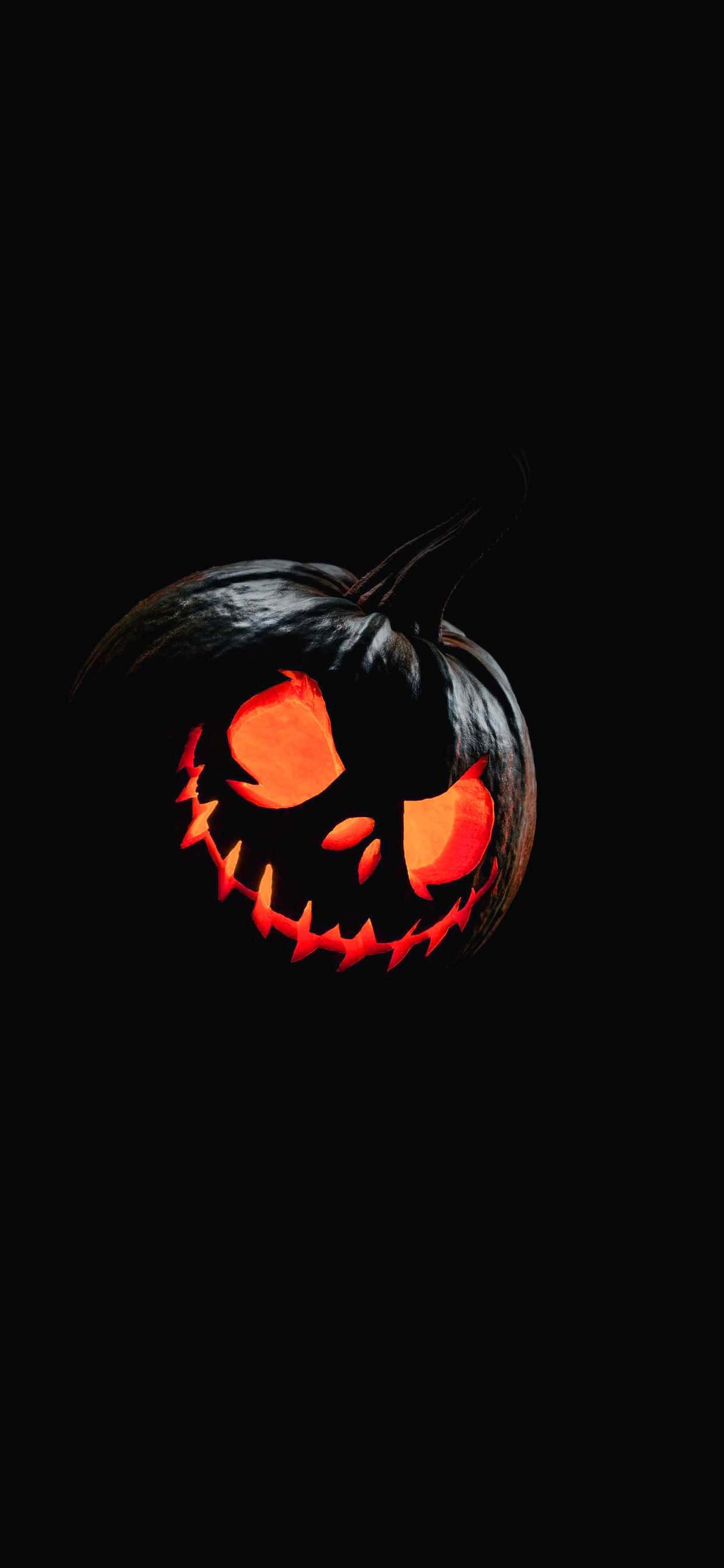 Halloween Pumpkin 桌布 壁紙 — 一個帶有發光橙色眼睛和鋸齒狀牙齒的可怕南瓜燈，在漆黑的背景中閃耀。