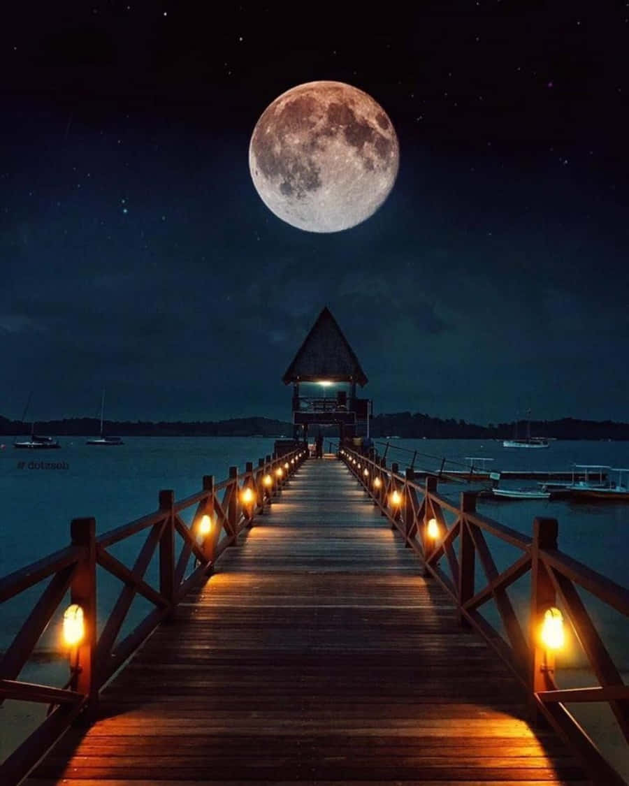 Beautiful Moon 桌布 壁紙 — 一個帶有發光燈籠的木製碼頭，在巨大的滿月和星空下，延伸向一個茅草屋頂的亭子。