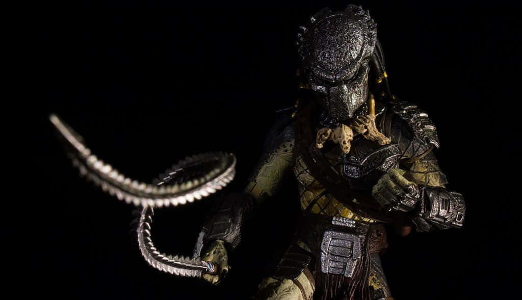 Wolf Predator 桌布 壁紙 — 一個帶有發光眼睛和尖刺尾巴的威脅性終極戰士動作人偶站在黑色背景前。
