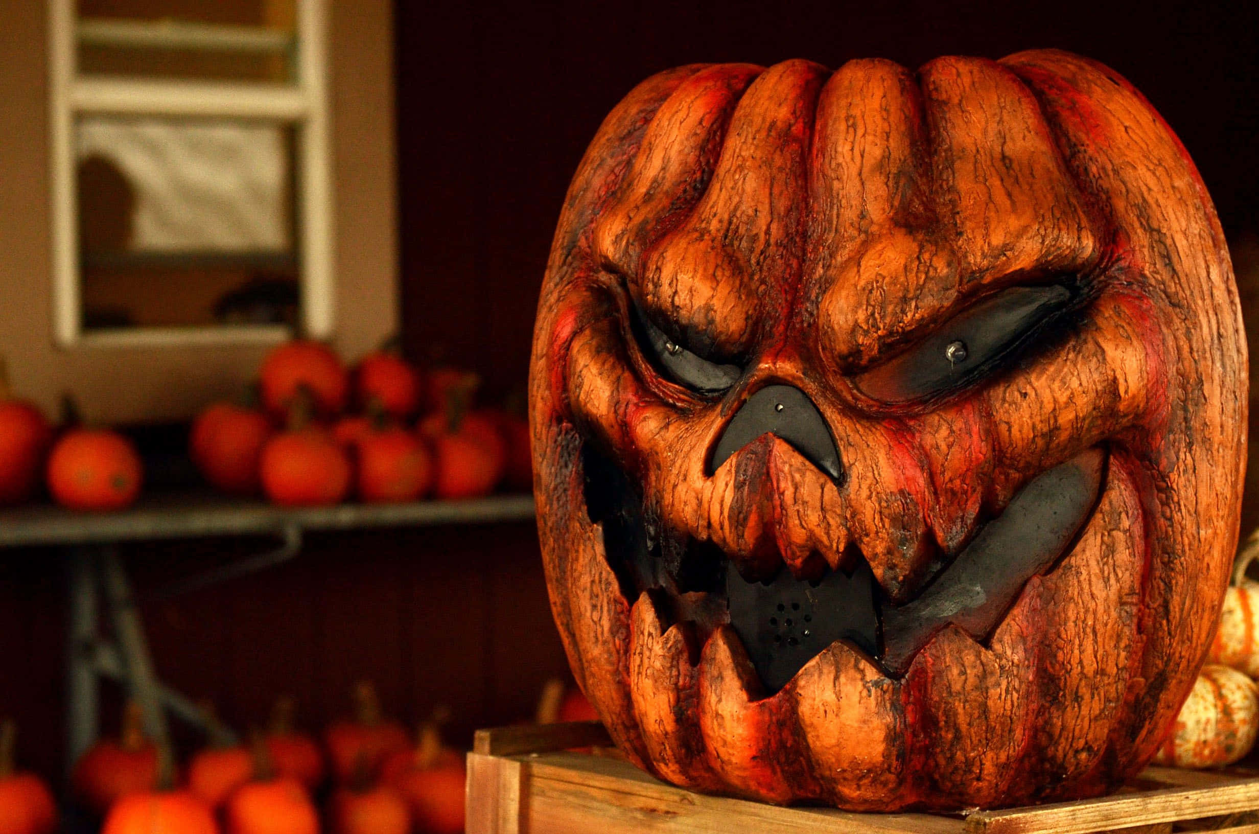 Halloween Pumpkin 桌布 壁紙 — 一個帶有發光眼睛和鋸齒狀牙齒的威脅性雕刻南瓜坐在一個木箱上，周圍環繞著較小的南瓜。