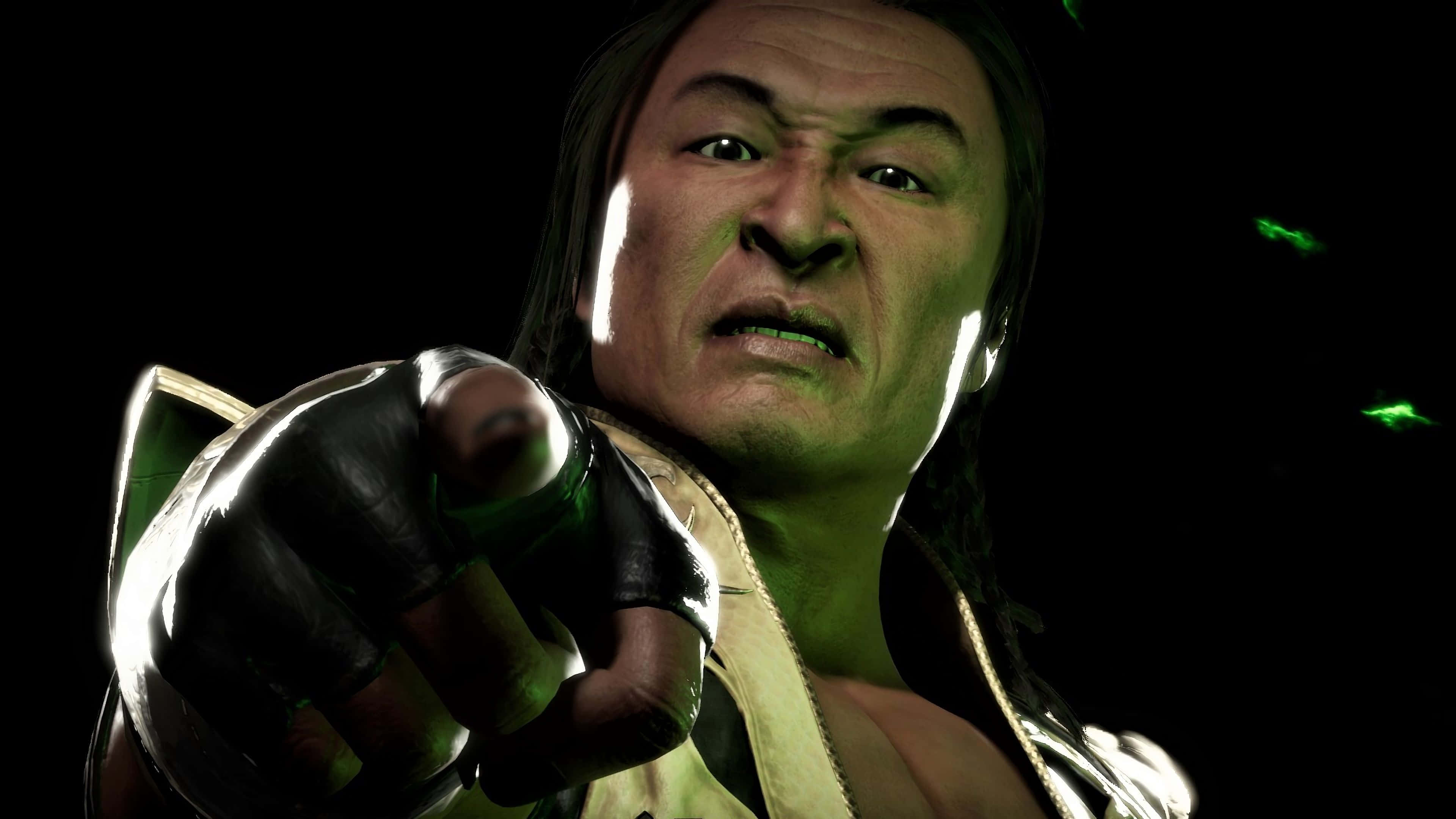 Mortal Kombat Shang Tsung 桌布 壁紙 — 一個帶有發光綠色皮膚的威脅性戰士，在黑暗背景中漂浮的綠色粒子襯托下，直接指向觀眾。
