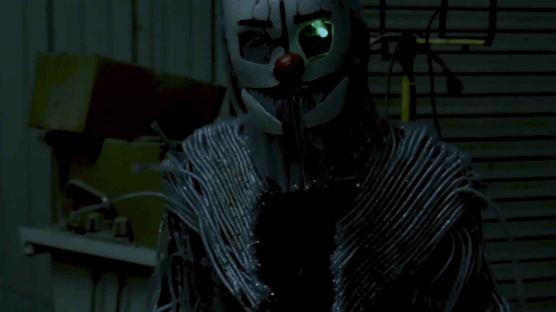 Ennard 桌布 壁紙 — 一個帶有發光綠色眼睛和裸露電線的可怕小丑，站在光線昏暗的工業房間裡。