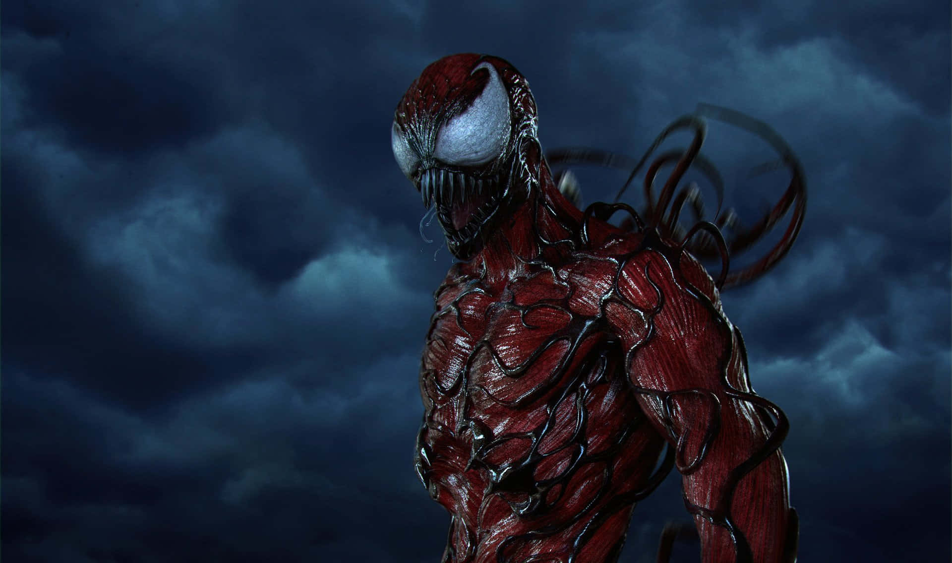 Carnage 桌布 壁紙 — 一個帶有白色眼睛和黑色觸手的威脅性紅色共生體生物，站在黑暗暴風雨的天空下。