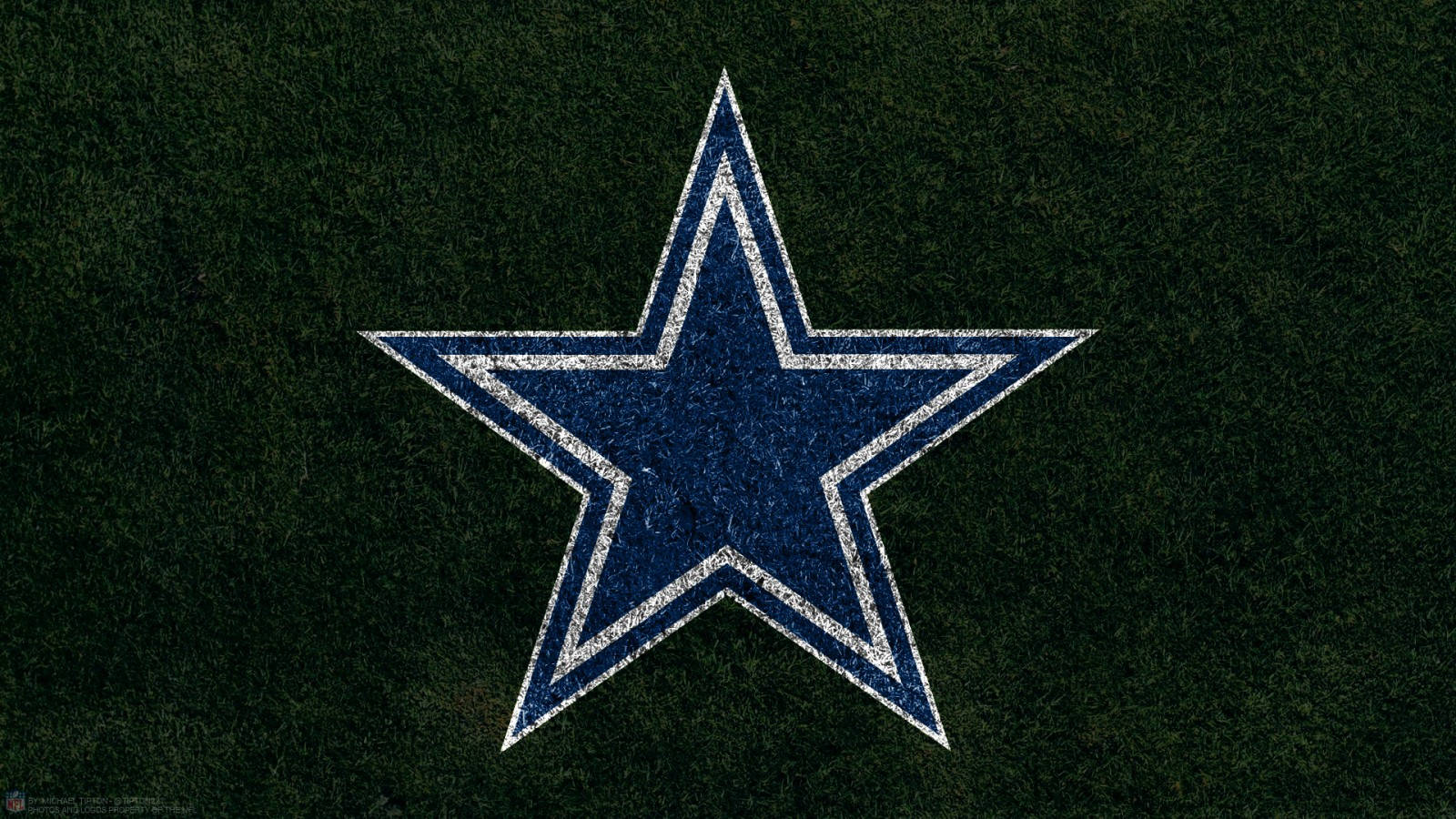 Dallas Cowboys Logo 桌布 壁紙 — 一個帶有白色輪廓的磨損藍色星星標誌，居中放置在深綠色草地紋理上。