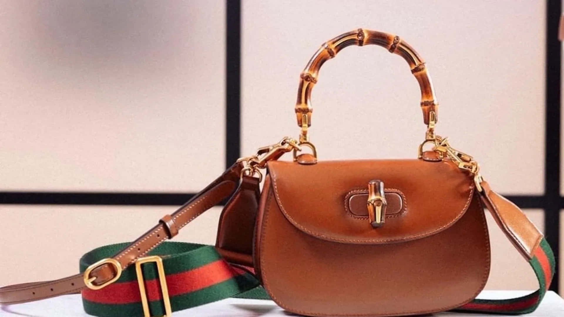 Gucci 桌布 壁紙 — 一個帶有竹手柄和綠紅條紋肩帶的棕褐色皮革Gucci手提包，放置在白色表面上，背景為簡約的米色和黑色。