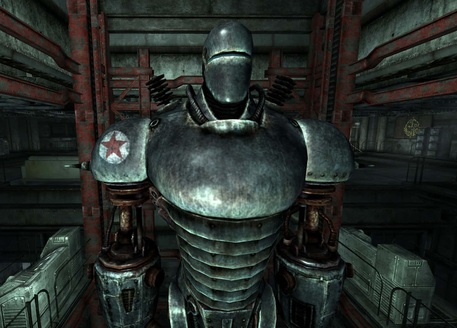 Liberty Prime 桌布 壁紙 — 一個帶有紅色星星標誌的高聳金屬機器人，站在一個有生鏽金屬橫樑的昏暗工業倉庫中。
