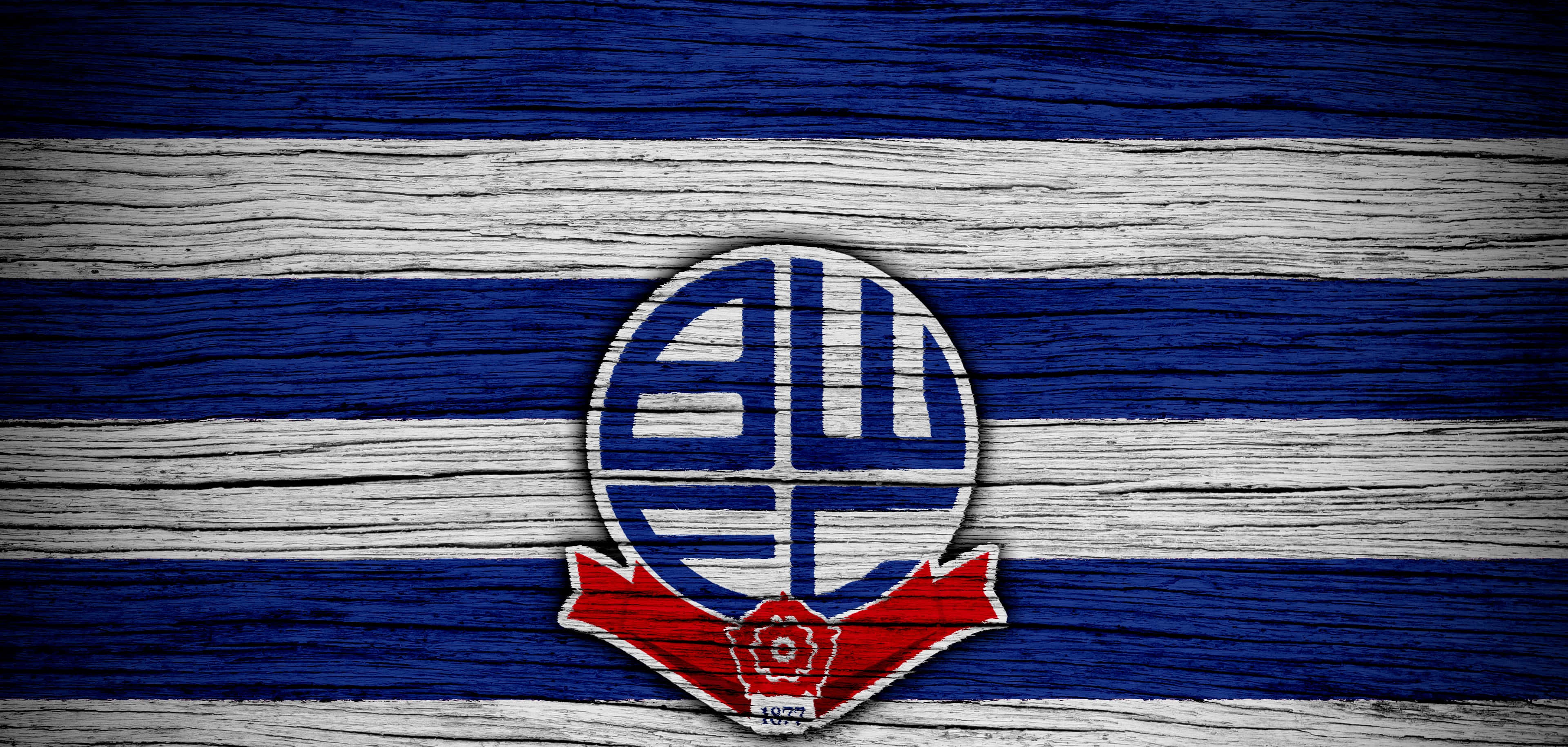 Bolton Wanderers Fc 桌布 壁紙 — 一個帶有紅色絲帶的藍白圓形徽章，放置在塗有藍白條紋的風化木板上。