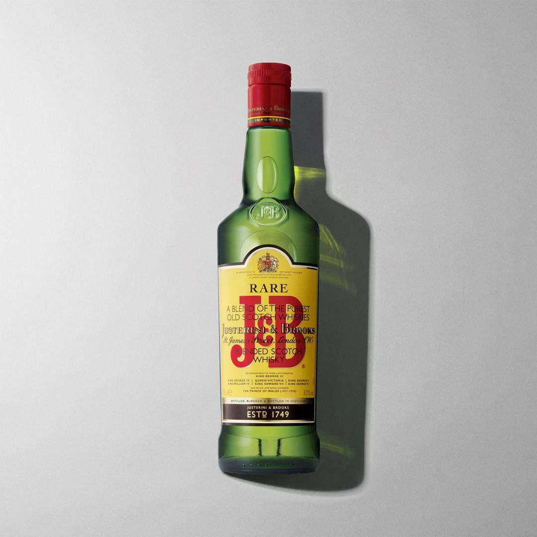 drinks 桌布 壁紙 — 一個帶有紅色蓋子的J&B Rare調和蘇格蘭威士忌綠色玻璃瓶，立在純灰色背景前，投射出清晰的陰影。