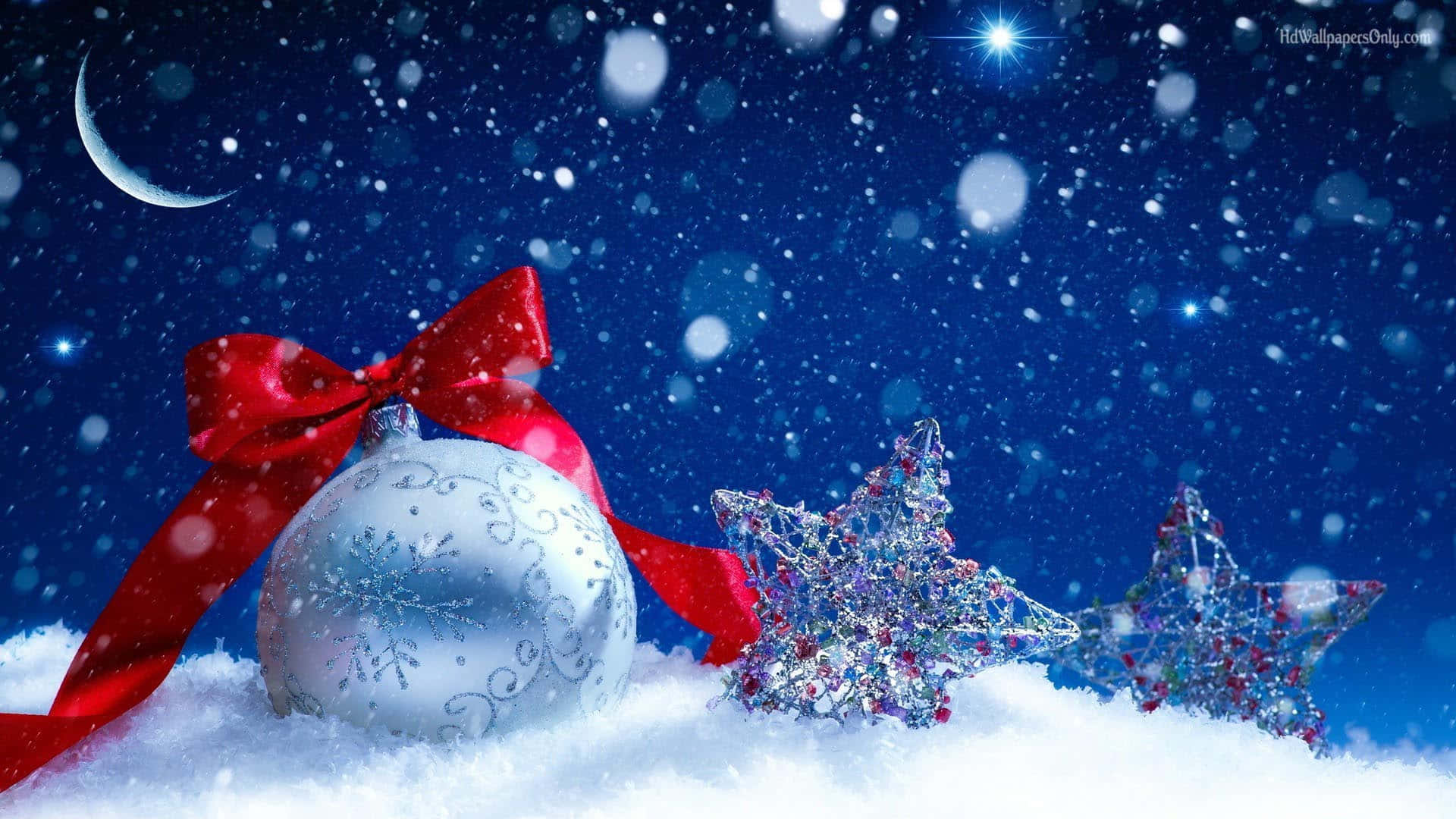 Christmas Winter Wonderland 桌布 壁紙 — 一個帶有紅色蝴蝶結和閃爍星星的銀色裝飾品，躺在新月和星空夜空下的雪地裡。