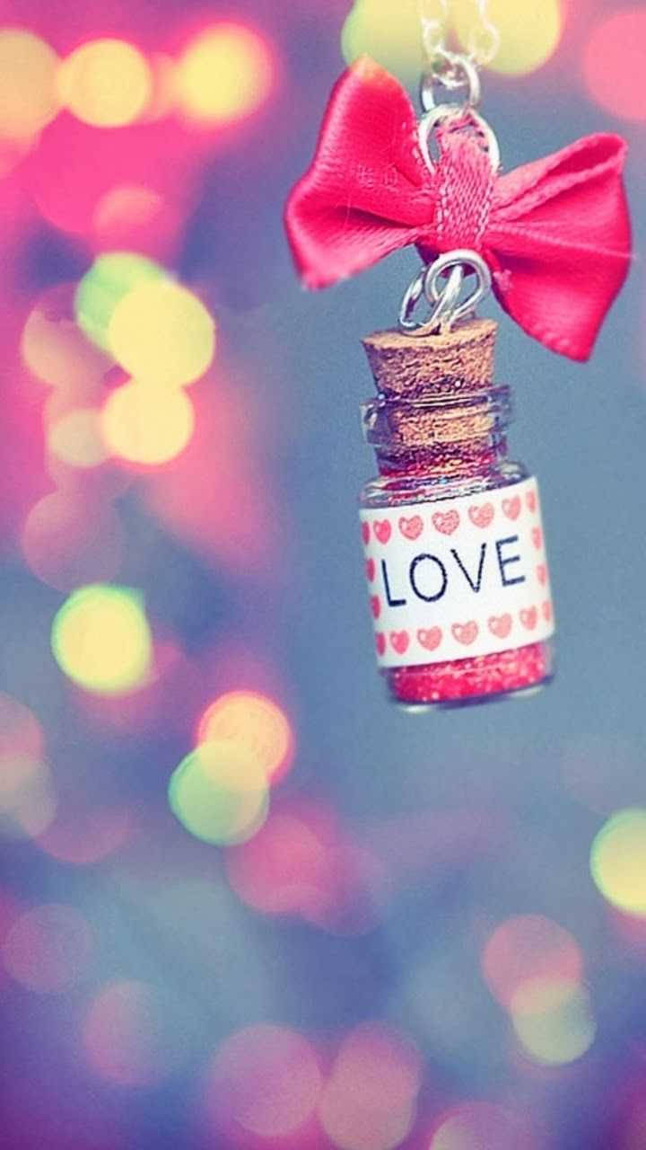 可愛女生 桌布 壁紙 — 一個帶有紅色蝴蝶結的小閃亮瓶子，標有LOVE，懸掛在彩色散景背景前。
