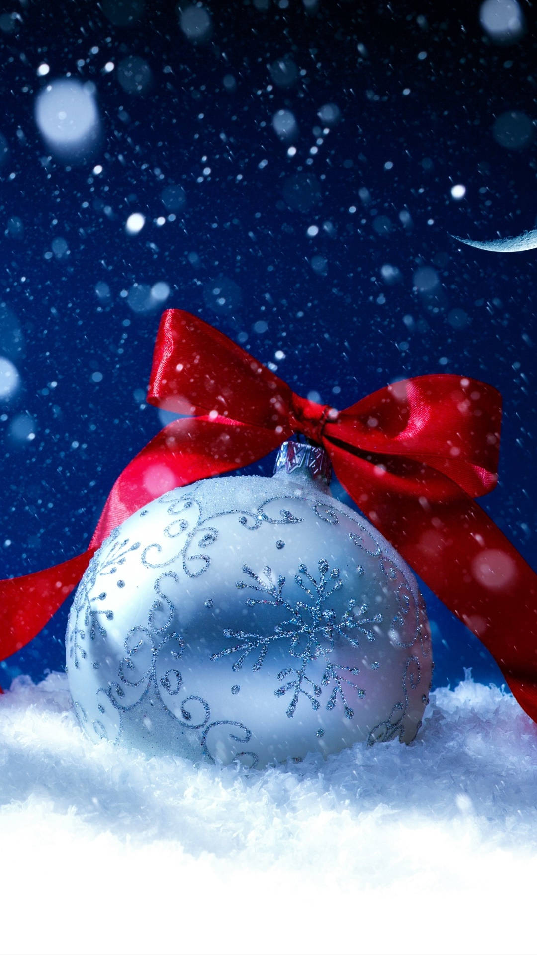 Snowy Christmas 桌布 壁紙 — 一個帶有紅色蝴蝶結的銀色雪花裝飾品，躺在雪地上，背景是繁星點點的夜空和飄落的雪花。