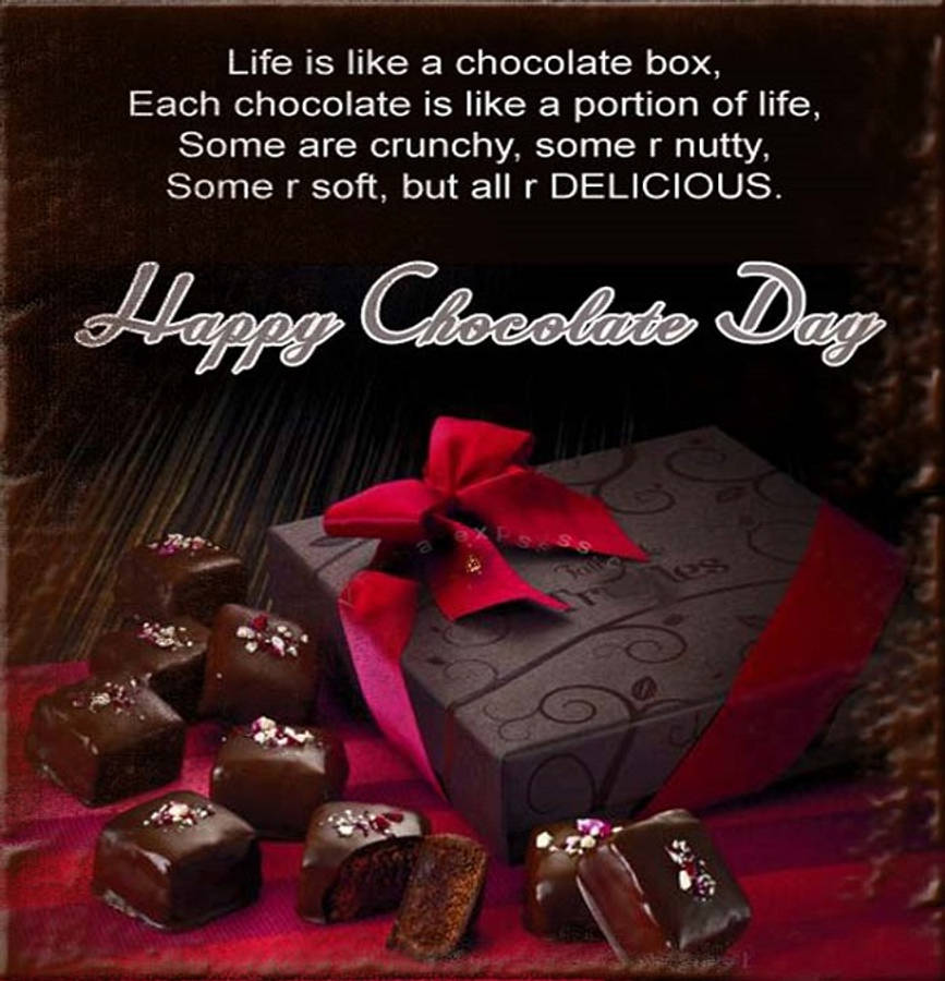 Chocolate Day 桌布 壁紙 — 一個帶有紅色蝴蝶結的黑巧克力禮盒，旁邊放著各式巧克力，放在一塊印有勵志語句的紅布上。