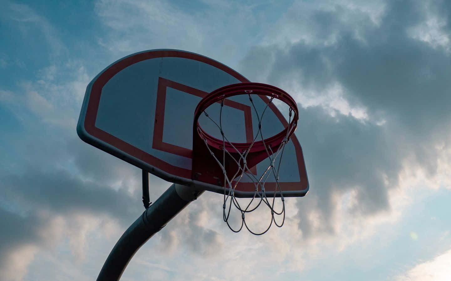 Basketball Aesthetic 桌布 壁紙 — 一個帶有紅色邊框和網的籃球框，在黃昏時分戲劇性的多雲天空下矗立。
