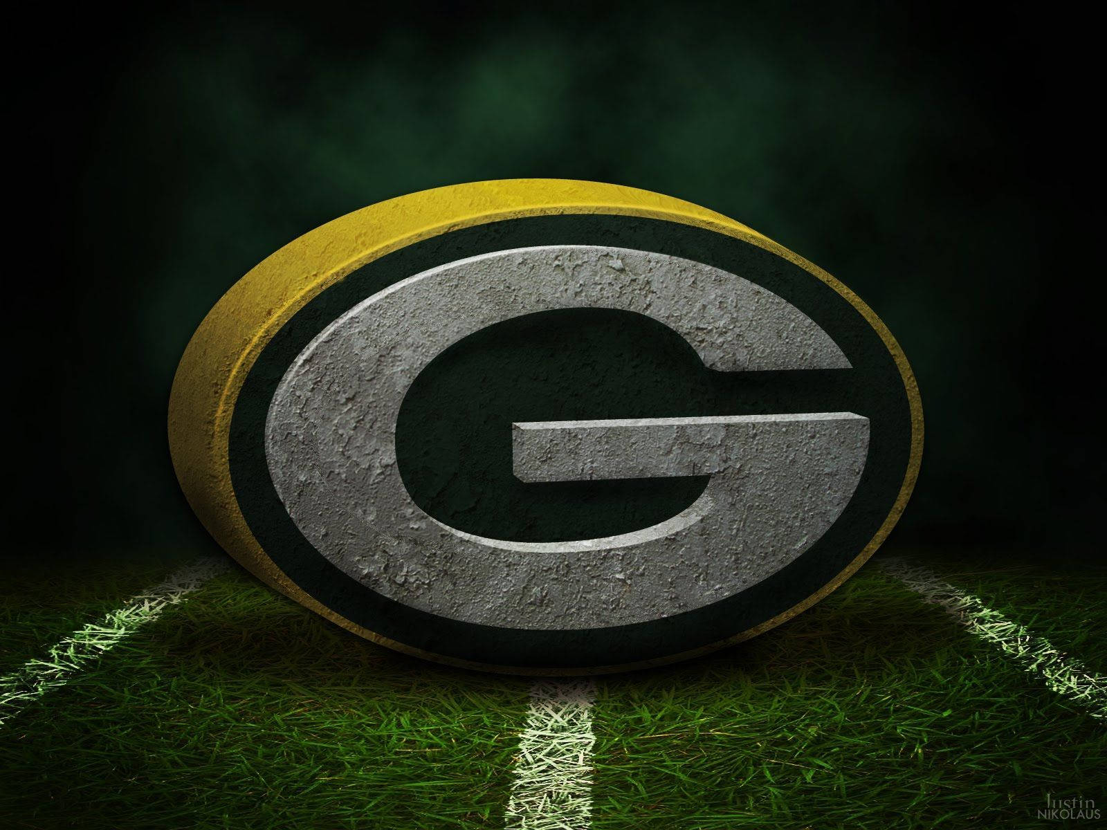 Packers 桌布 壁紙 — 一個帶有紋理的 Green Bay Packers 標誌放置在一個有白色碼線的草地足球場上，光線效果戲劇性。