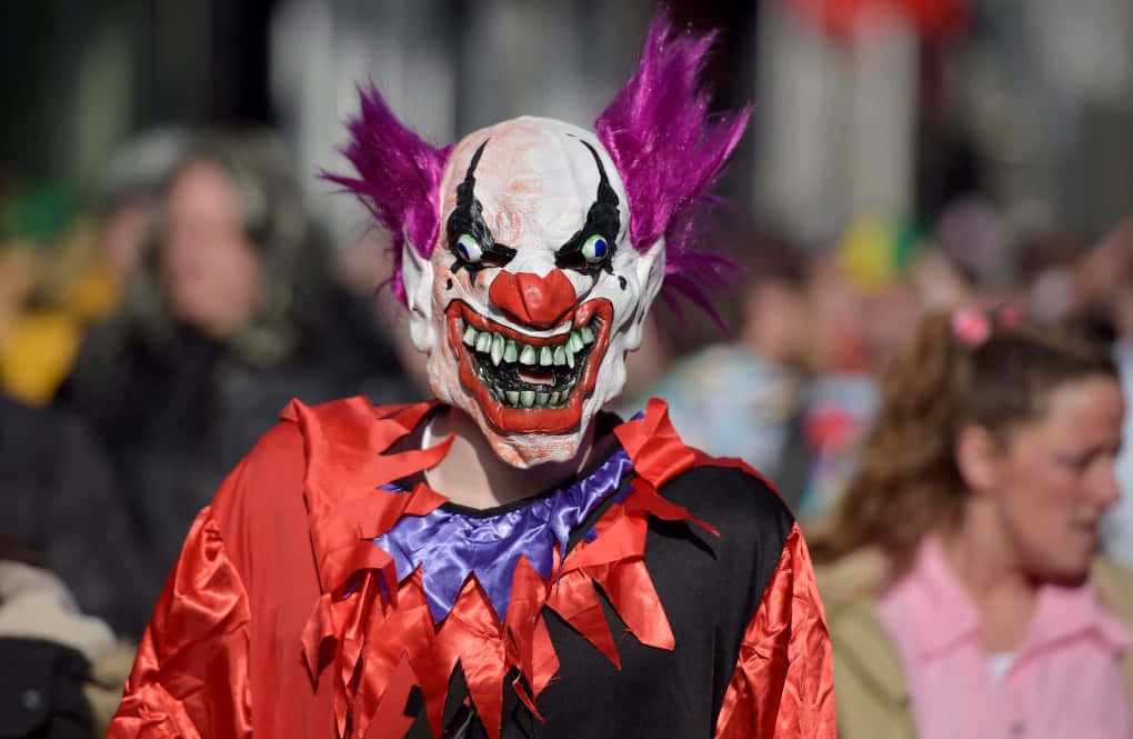 Creepy Clown 桌布 壁紙 — 一個帶有紫色頭髮和紅色鼻子的威脅小丑在擁擠的街道上凝視著鏡頭。
