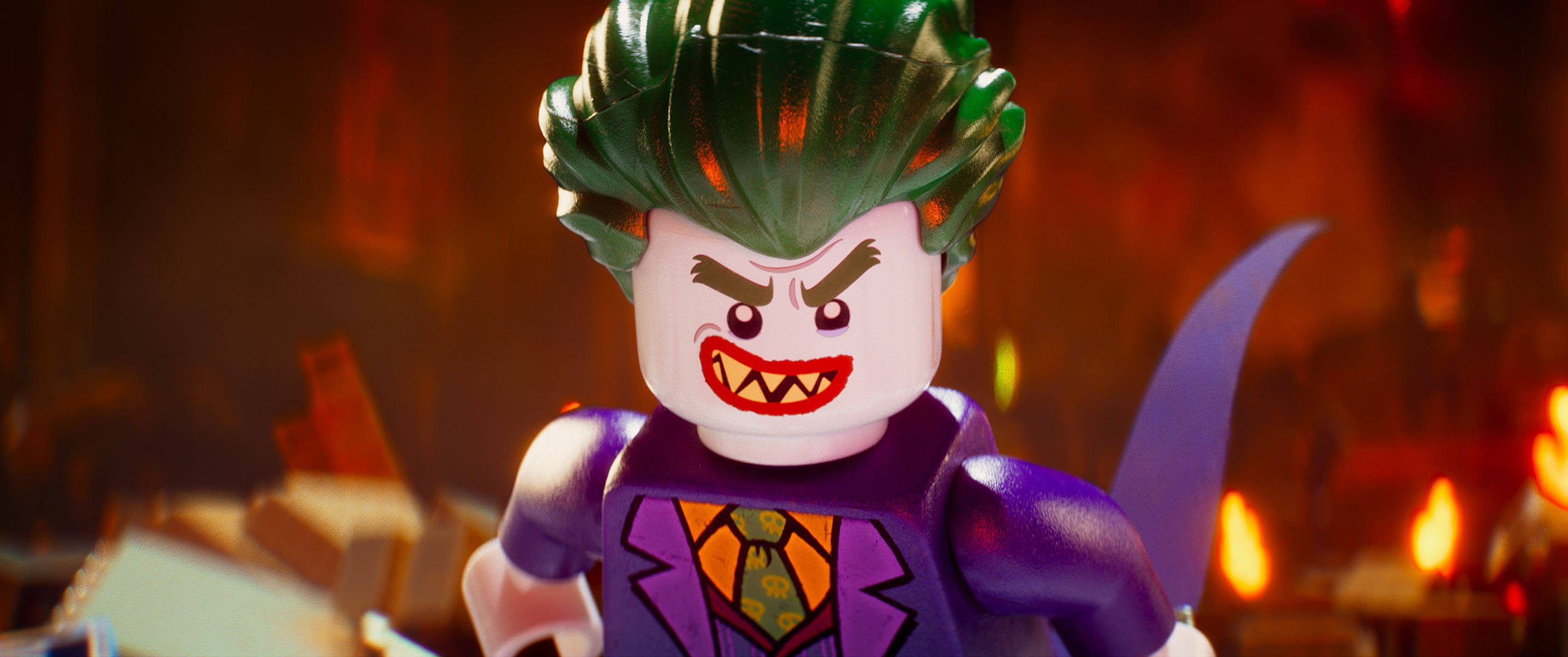 Digital 桌布 壁紙 — 一個帶有綠色頭髮和紫色西裝的威脅性LEGO小丑站在火熱混亂的背景中。