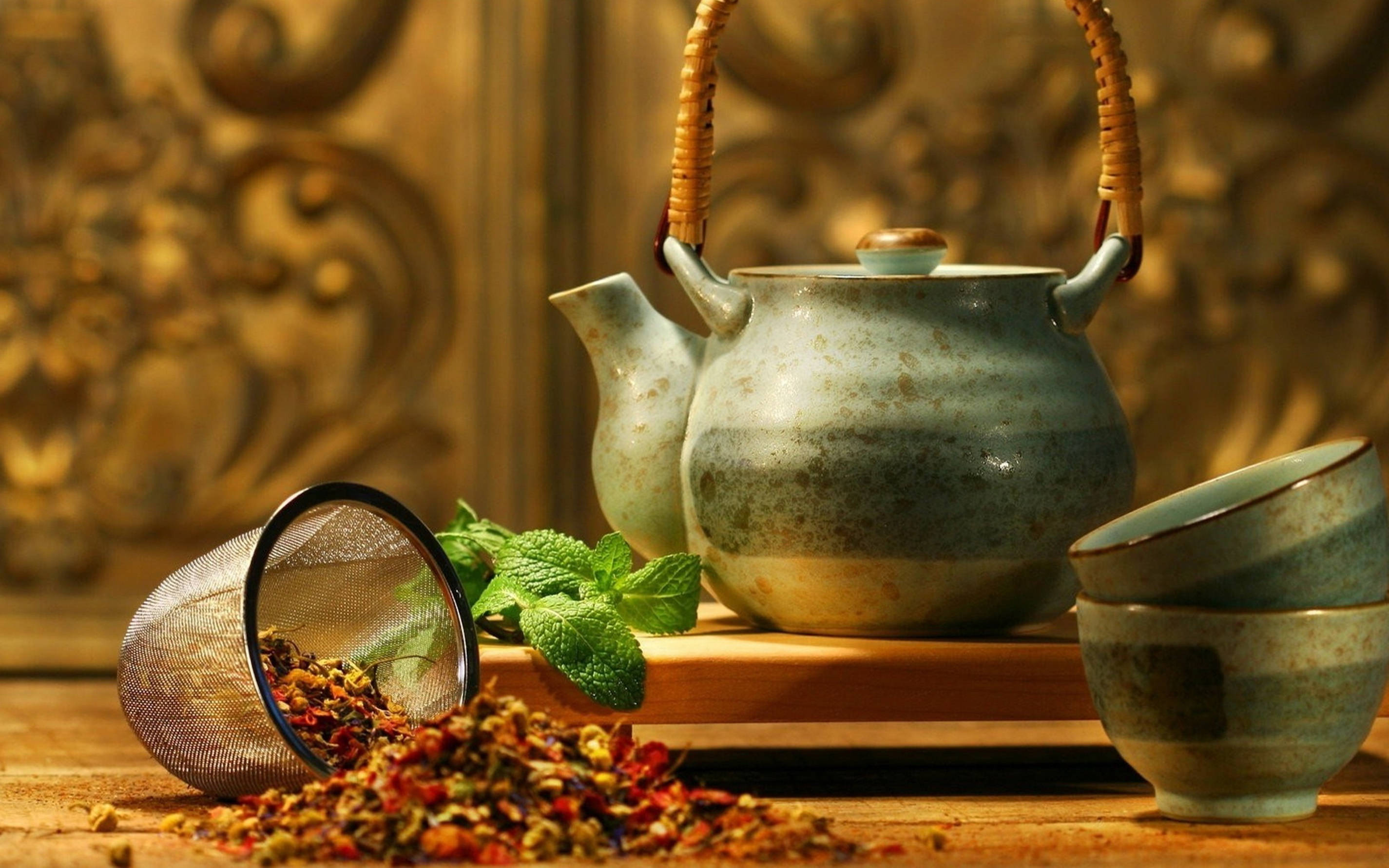 設計 桌布 壁紙 — 一個帶有編織手柄的鄉村風格陶瓷茶壺，旁邊放著疊起的杯子和灑落的乾香草，在木桌上。