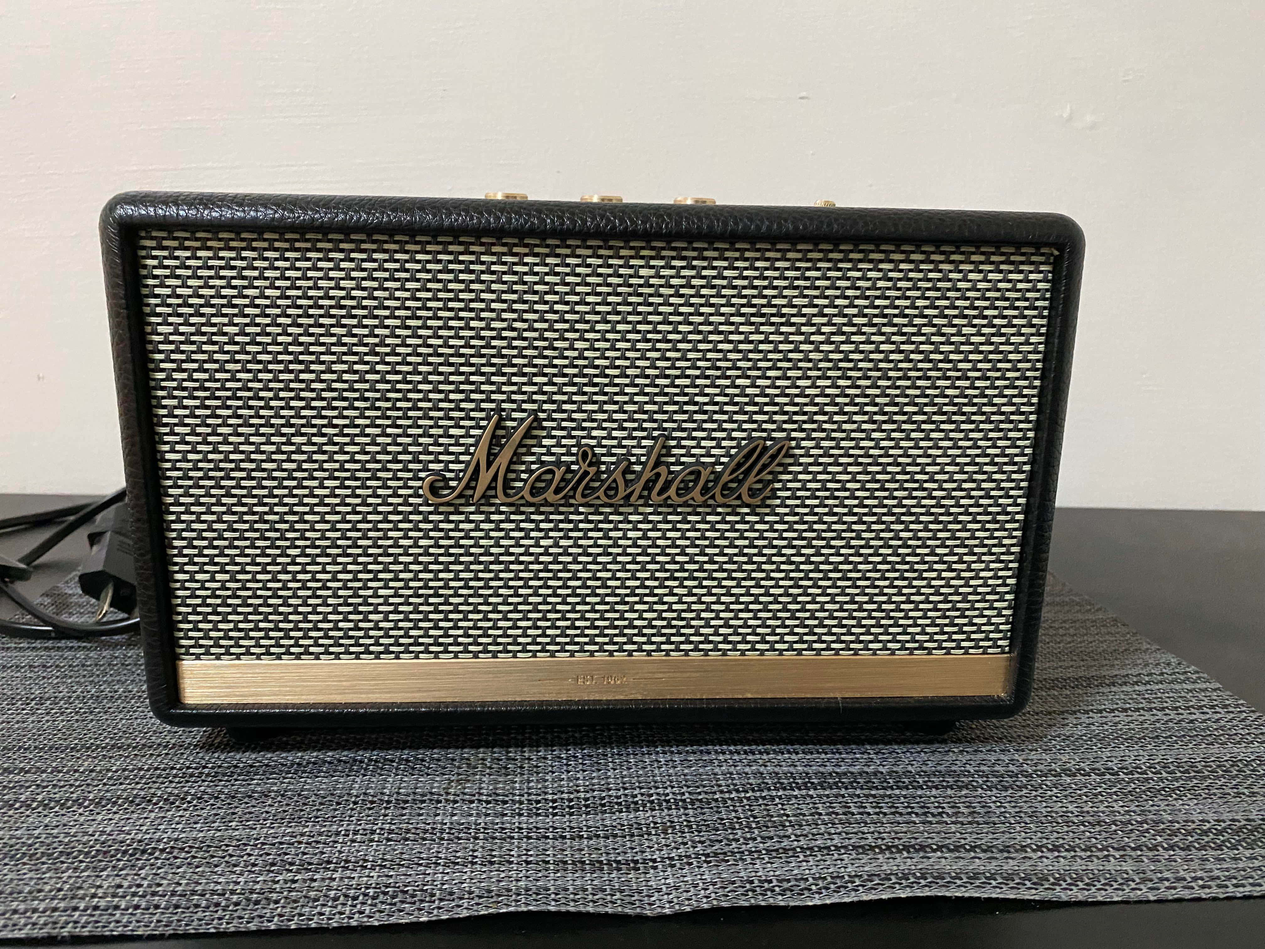 Marshall 桌布 壁紙 — 一個帶有編織網格和金色飾邊的Marshall揚聲器，放置在灰色紋理墊上，背景是純白牆壁。