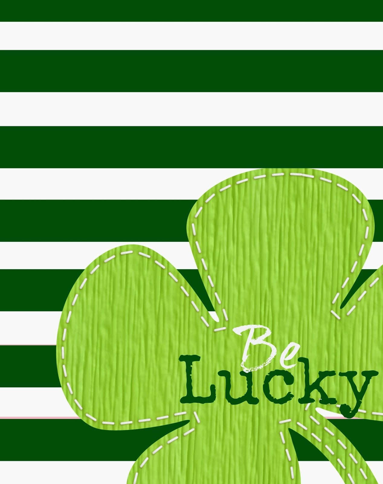 Saint Patricks Day 桌布 壁紙 — 一個帶有縫合邊緣和「Be Lucky」文字的亮綠色三葉草漂浮在鮮明的綠色和白色水平條紋上。