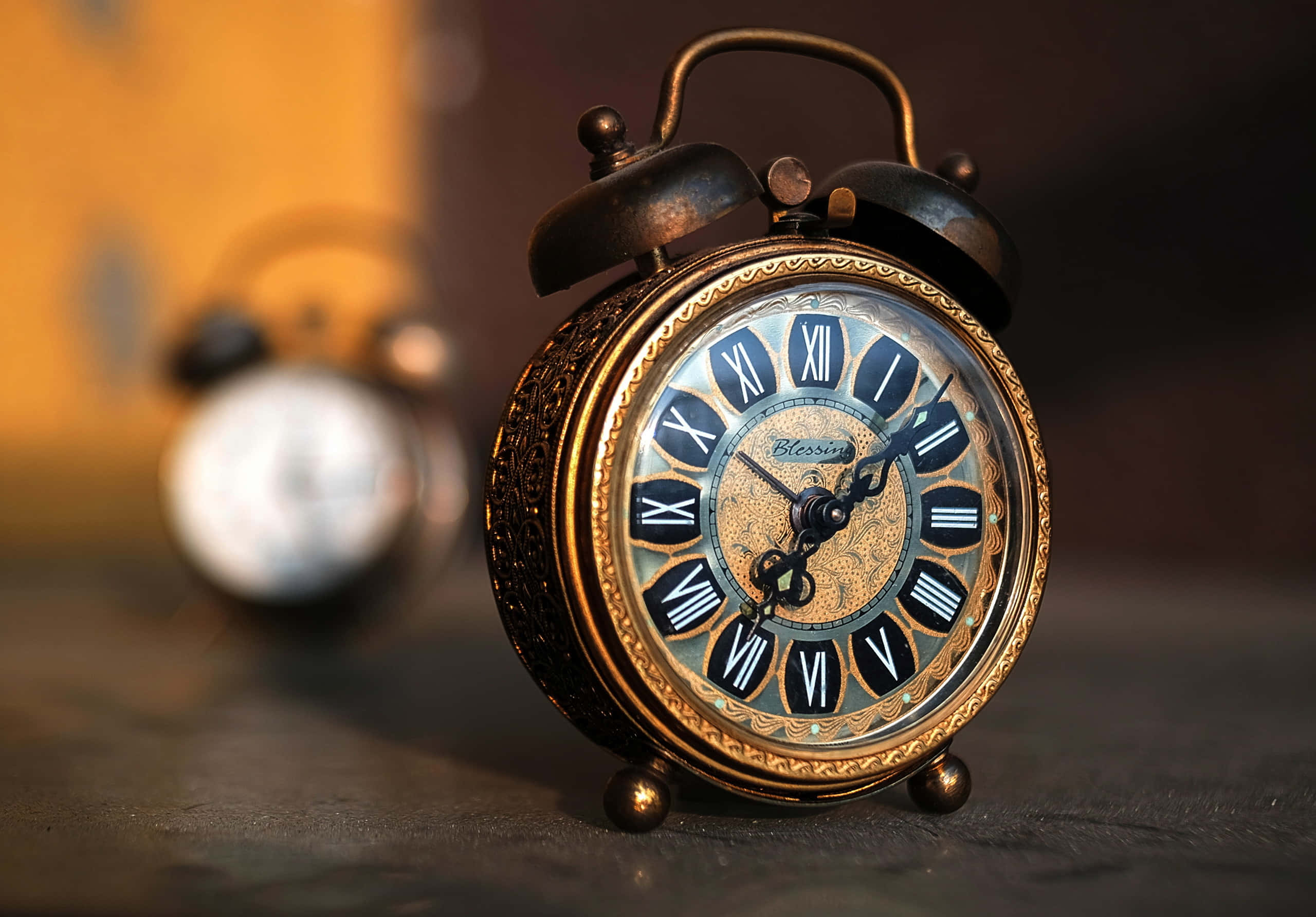 Clock 桌布 壁紙 — 一個帶有羅馬數字和華麗細節的復古黃銅鬧鐘，放置在黑暗表面上，沐浴在溫暖的金色光線中。