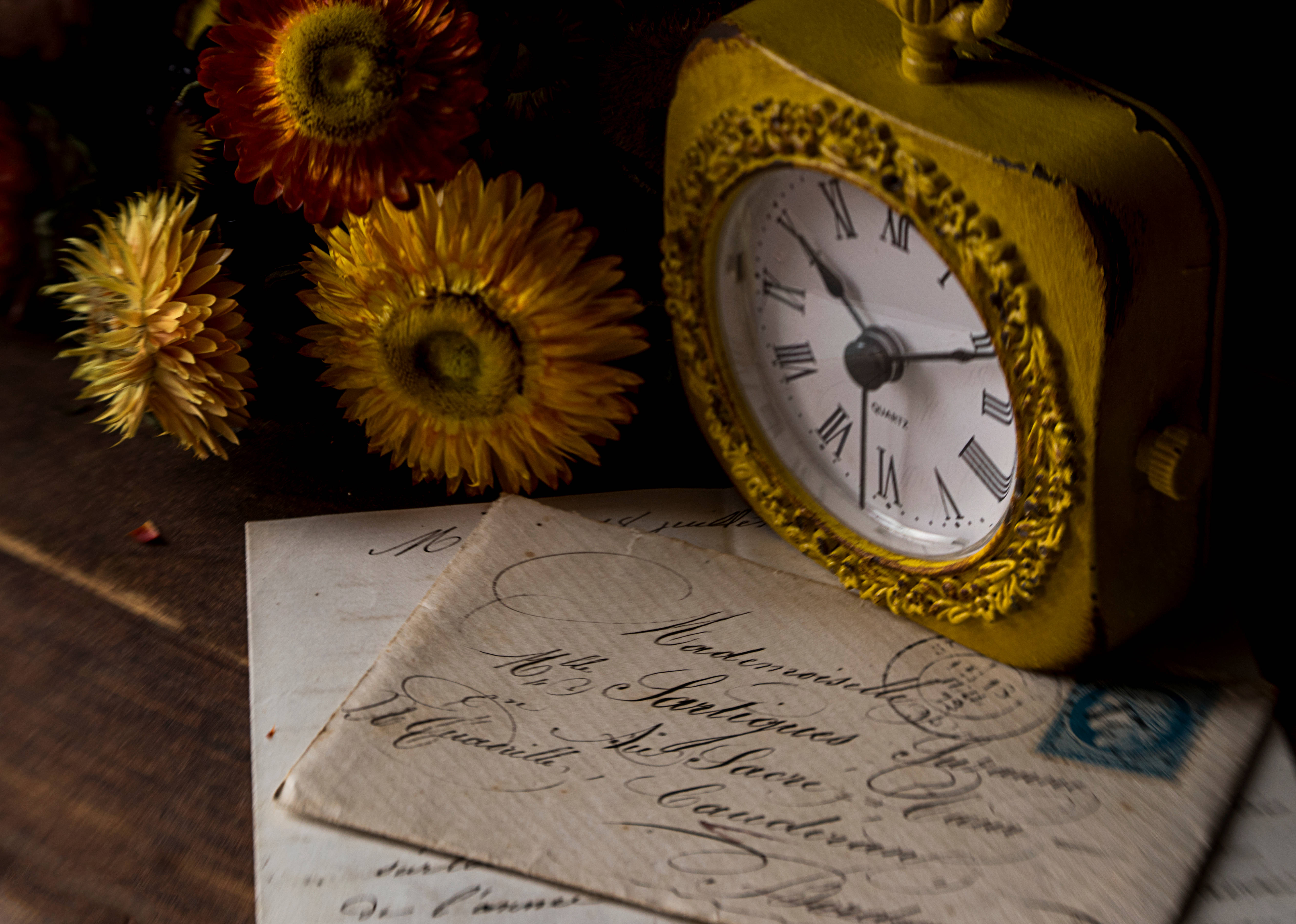 Clock 桌布 壁紙 — 一個帶有羅馬數字的復古黃色時鐘，旁邊放著乾花和古董信件，置於木質表面上。