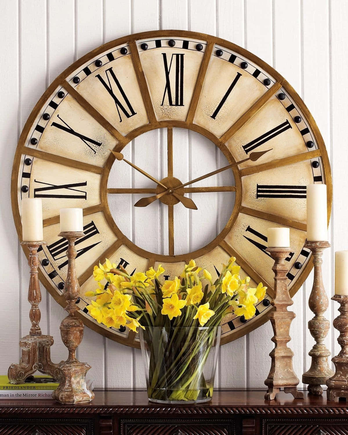 Wall Clock 桌布 壁紙 — 一個帶有羅馬數字的鄉村風格復古時鐘掛在白色鑲板牆上，下方深色木質玄關桌上擺放著黃色水仙花和燭台。