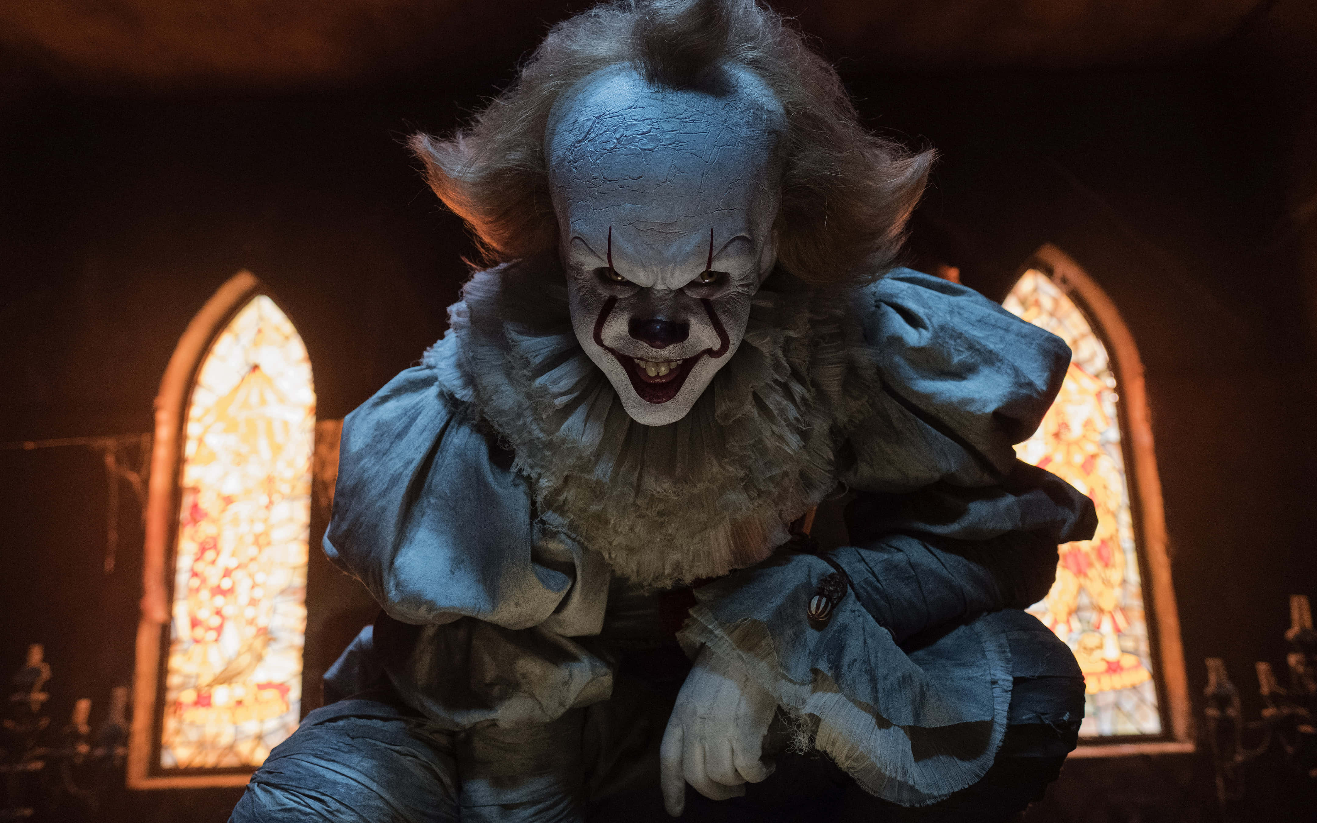 It 2017 桌布 壁紙 — 一個帶有蒼白妝容和狂野頭髮的威脅性小丑蹲在光線昏暗的教堂裡，背後彩色玻璃窗閃耀著光芒。